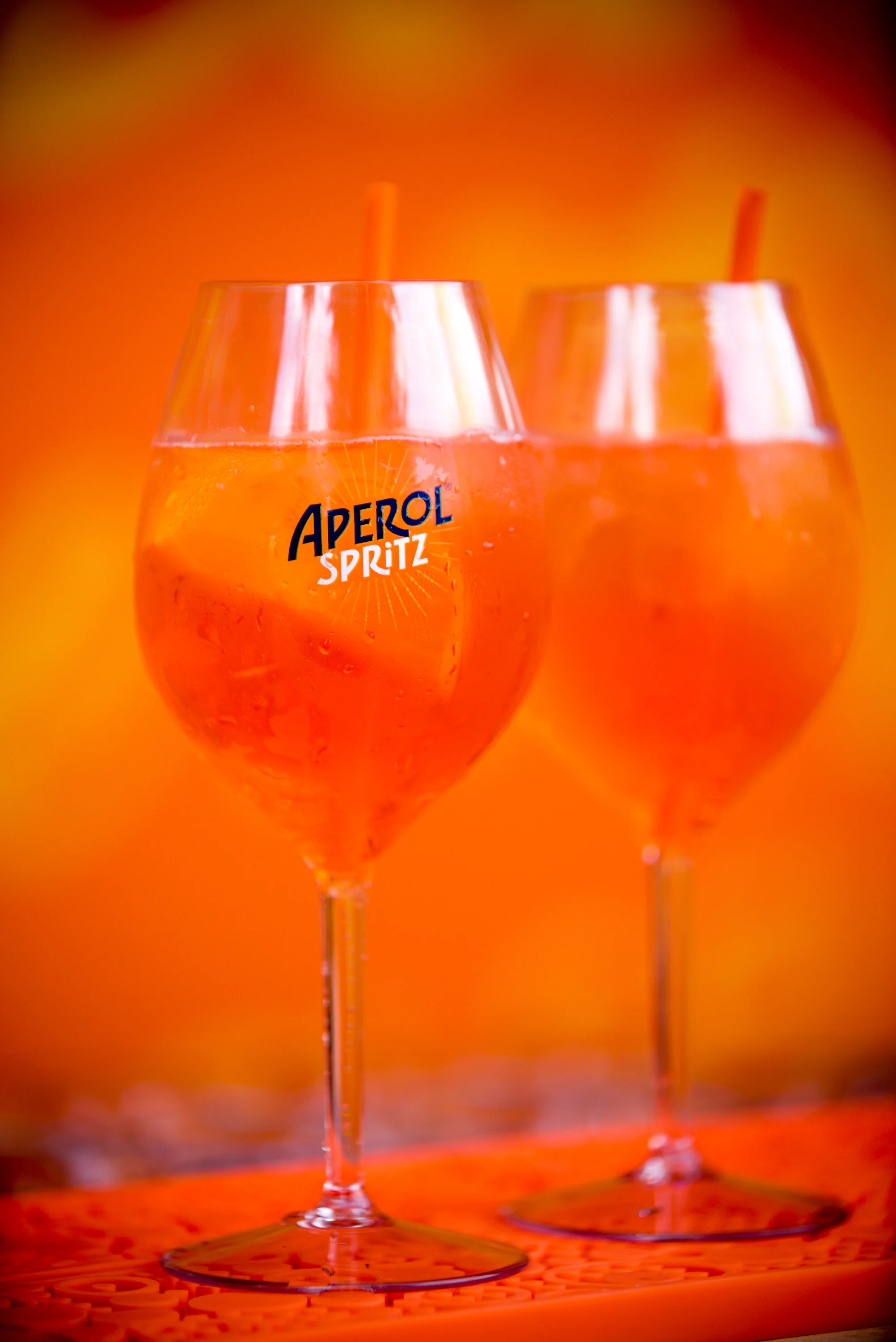 Deux verres de cocktail Aperol Spritz avec des yeux d'orange et une petite paille, fondu en arrière-plan dans des teintes chaudes.