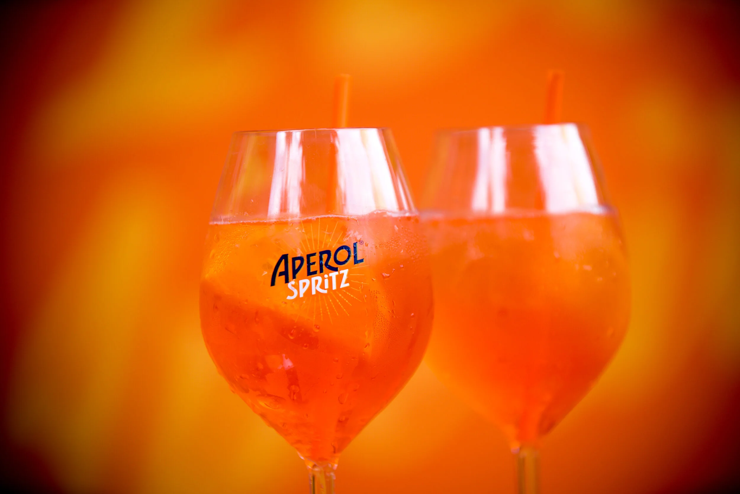 Deux verres remplis d'Aperol Spritz avec des citrons dans un fond orange flou.