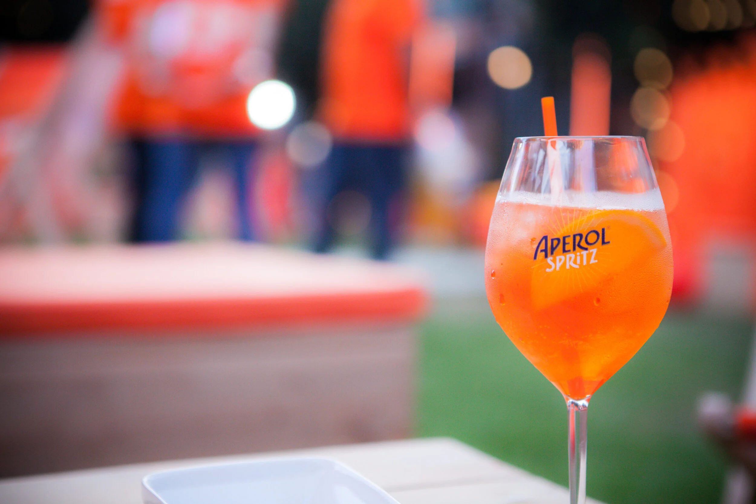 Verre de soda Aperol Spritz avec tranche d'orange et paille orangée, flou d'arrière-plan.