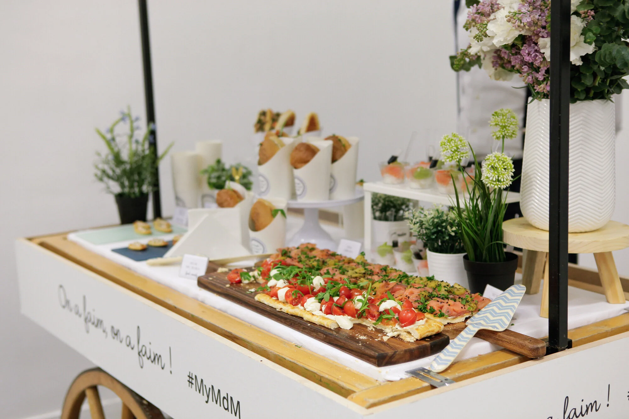 Buffet avec des canapés, une pizza et des fleurs en pot, dans un décor blanc et bois.