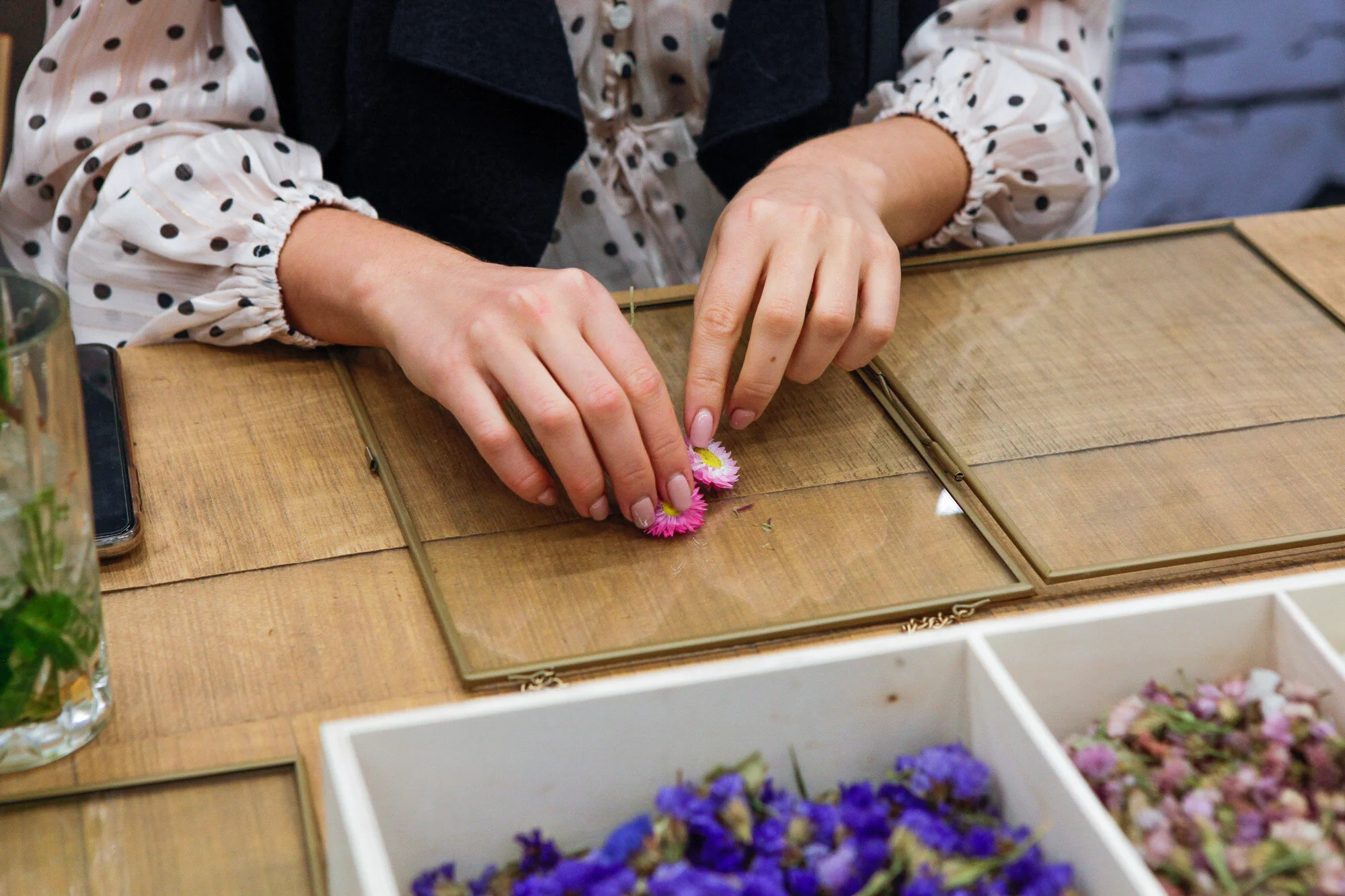 Une personne arrange des fleurs colorées sur une surface en bois, avec des fleurs en vrac dans une boîte en devant.