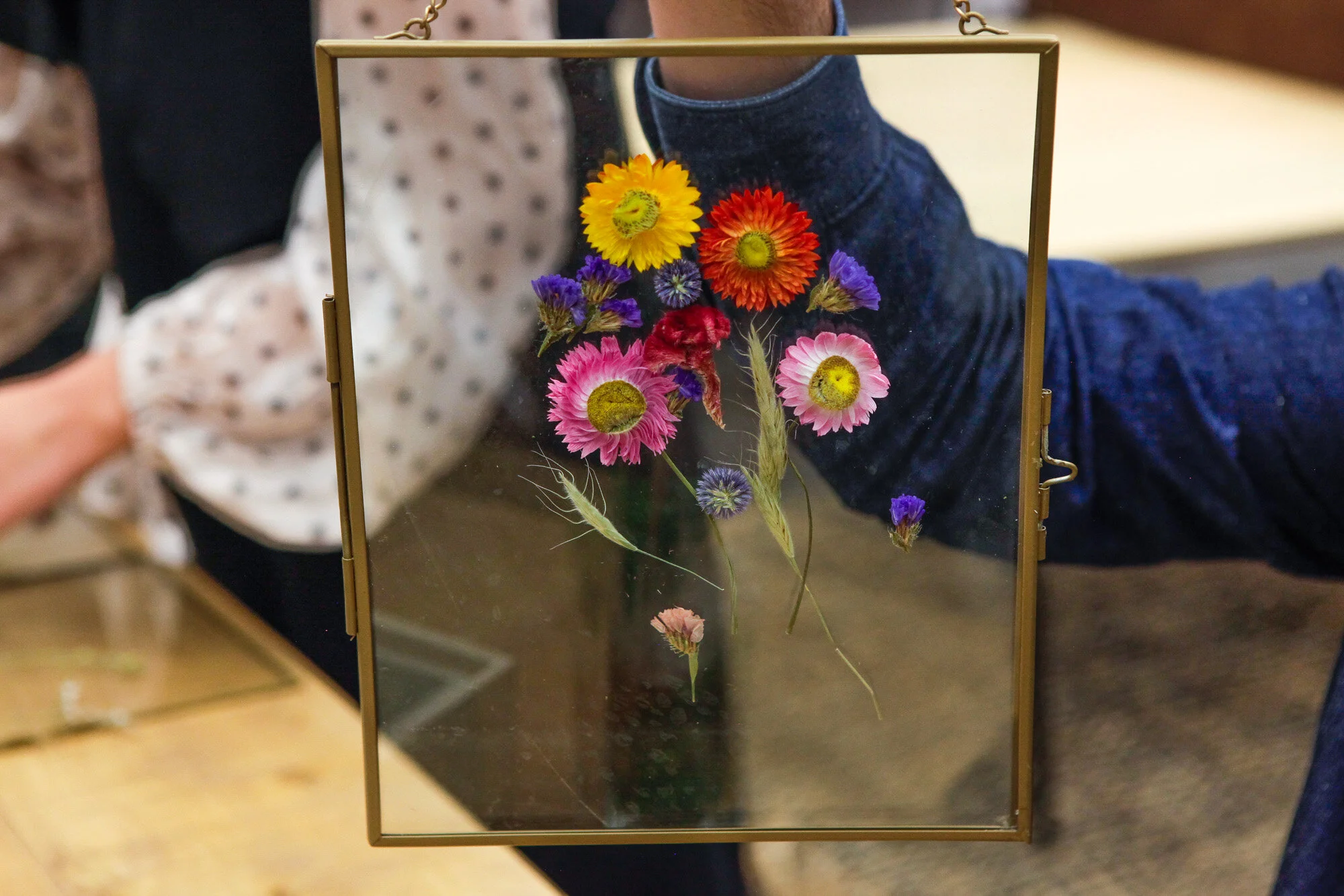 Un cadre en verre contenant une composition de fleurs séchées colorées, vue de face