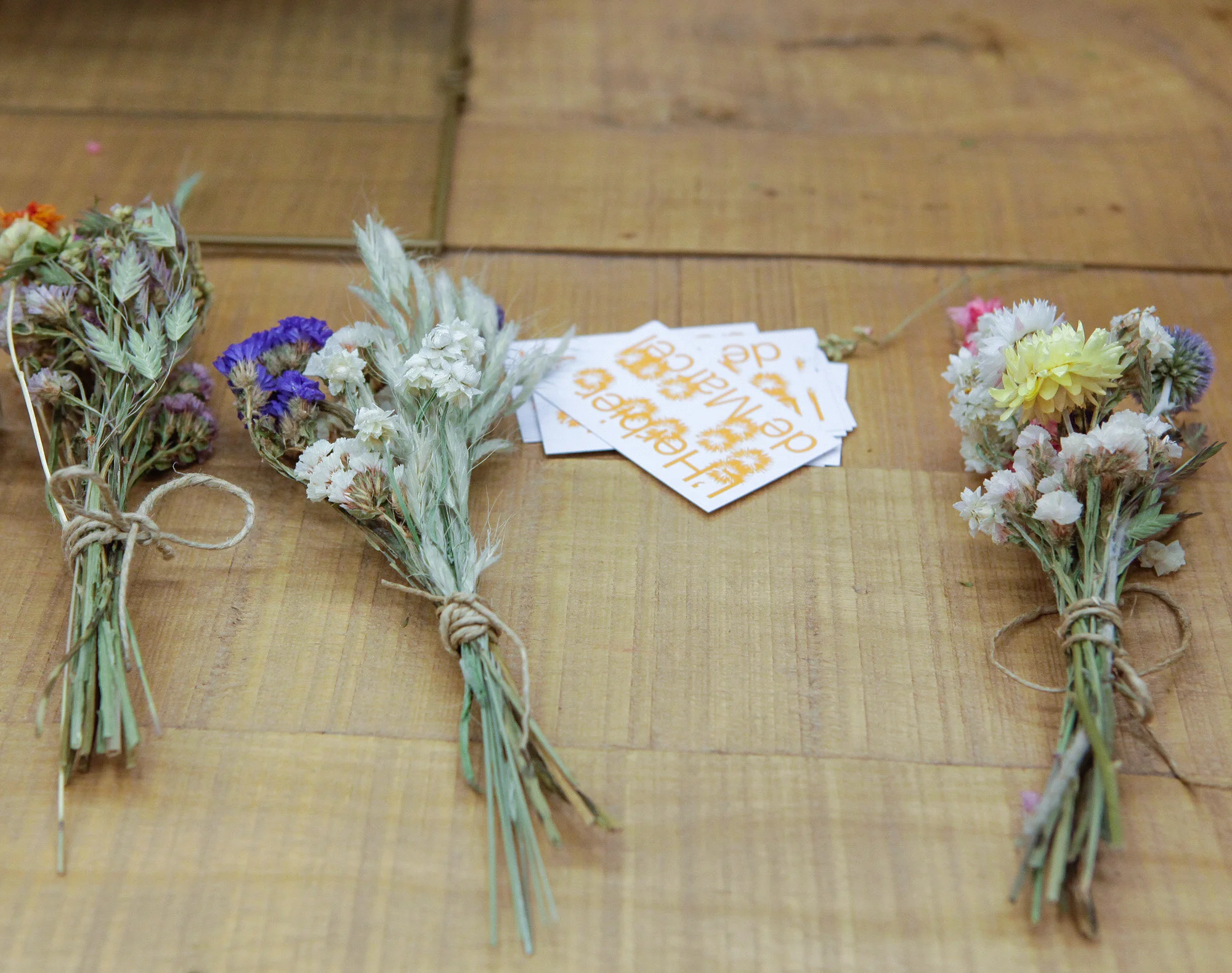 Trois bouquets de fleurs séchées attachés avec de la ficelle, disposés en ligne sur une surface en bois.