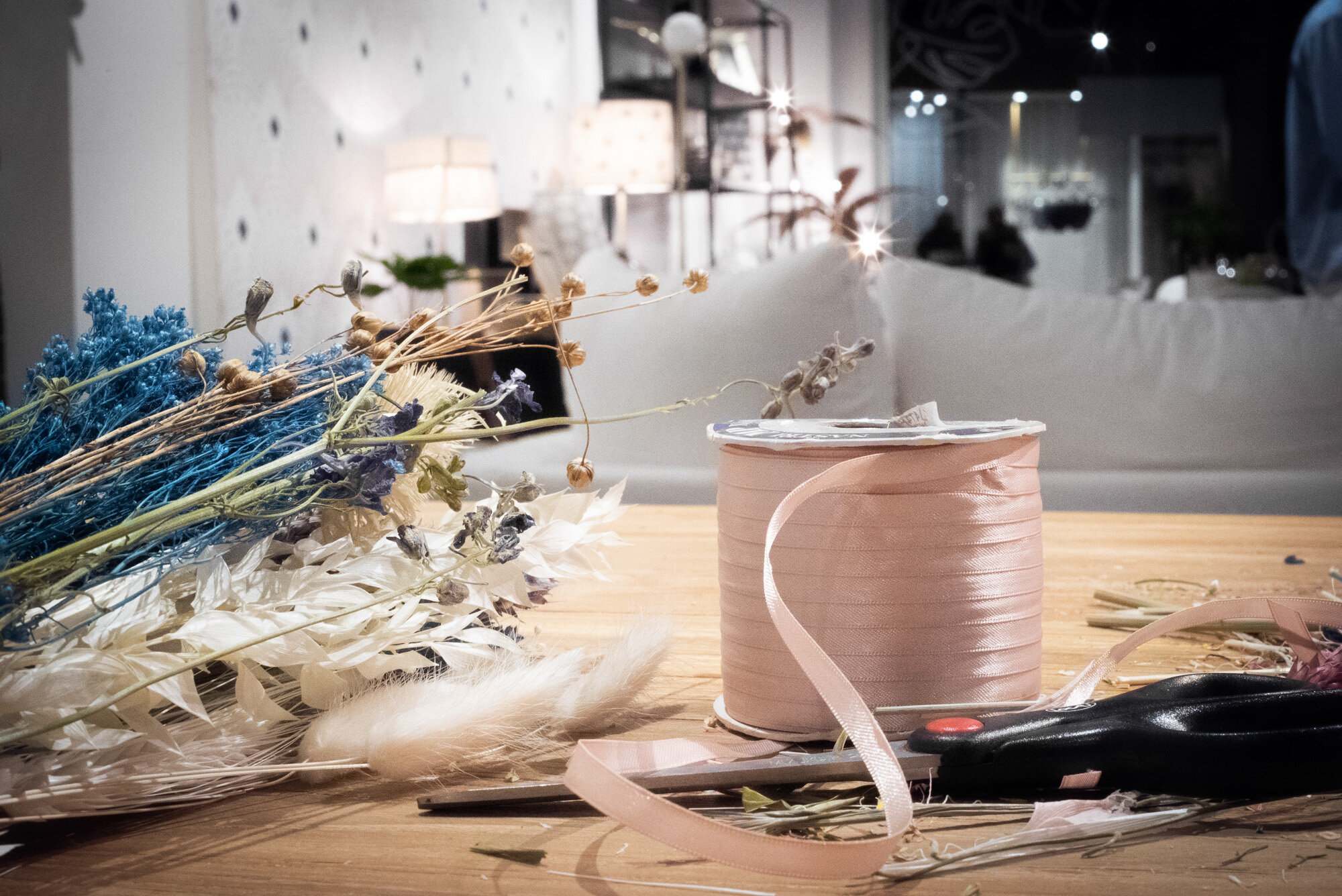 Fleurs séchées, bobine de ruban de satin rose, ciseaux sur une table en bois, dans un intérieur décoré.