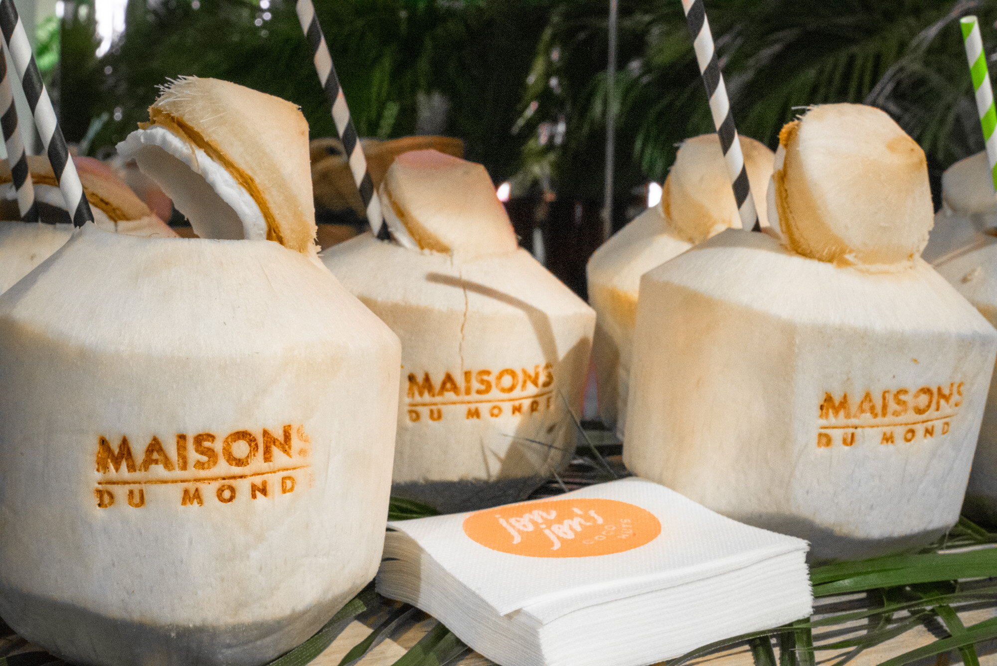 des noix de coco fraîches avec des pailles en plastique et des serviettes jetables portant le logo 'Maisons du Monde'
