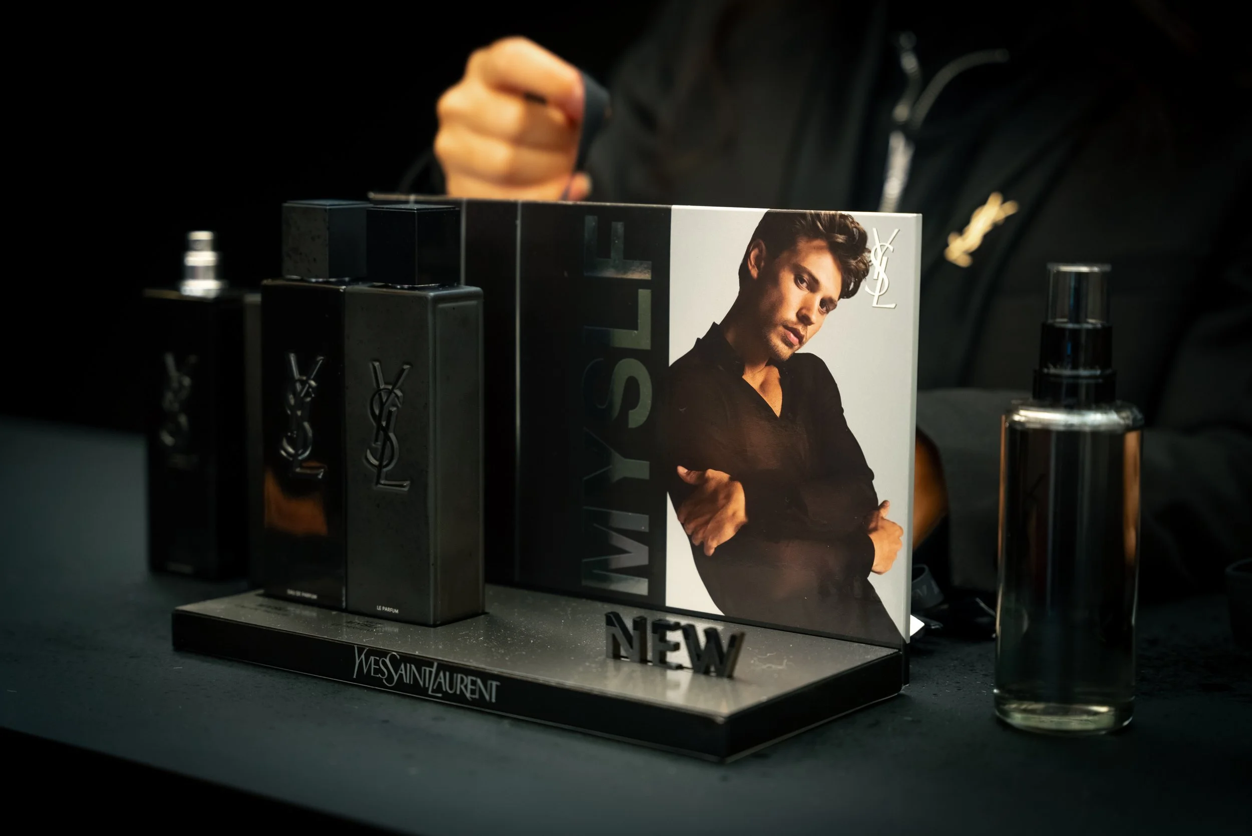 Une présentation de parfums Yves Saint Laurent avec flacons noirs et une affiche avec un homme dans un cadre noir et blanc