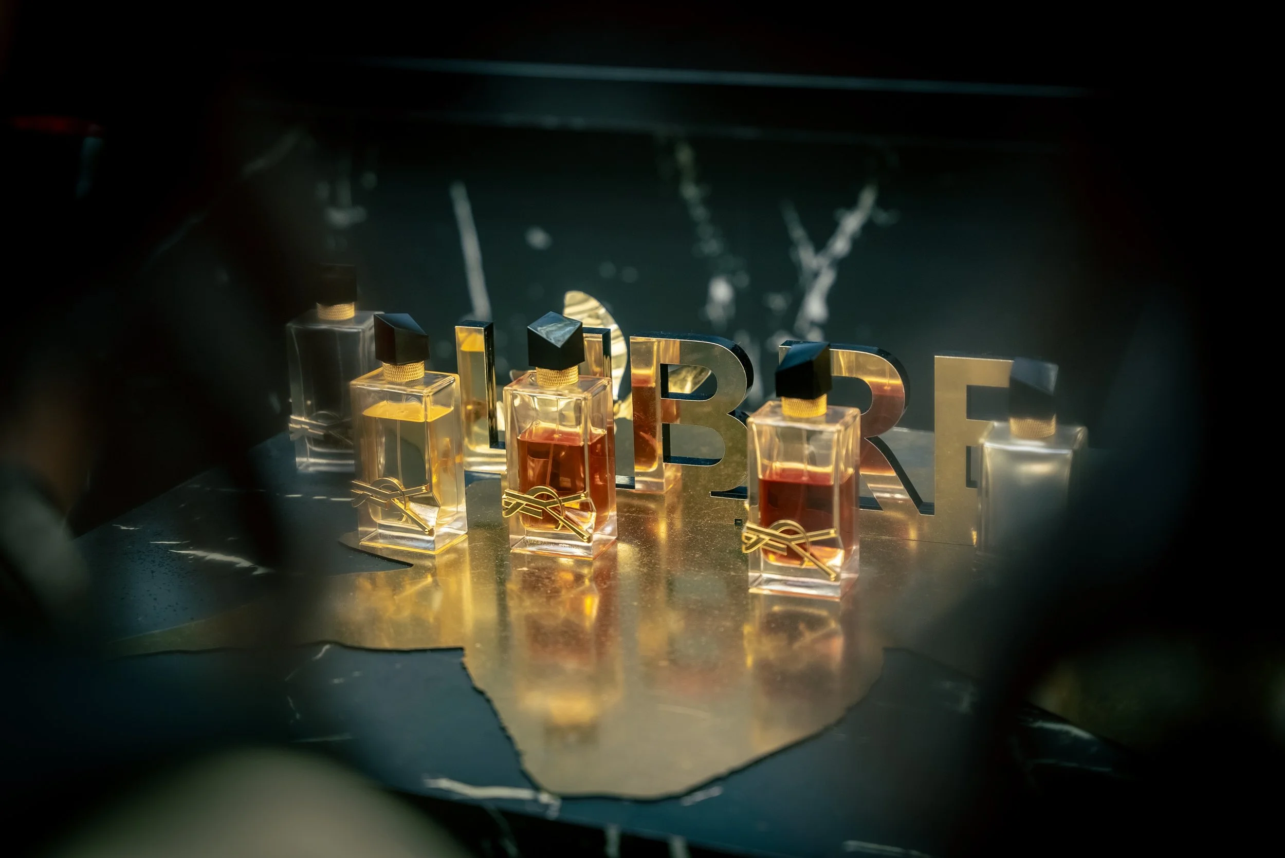 Préludes de parfums avec flacons en verre et lettres en métal formant le mot 'LIBRE' sur une surface en or