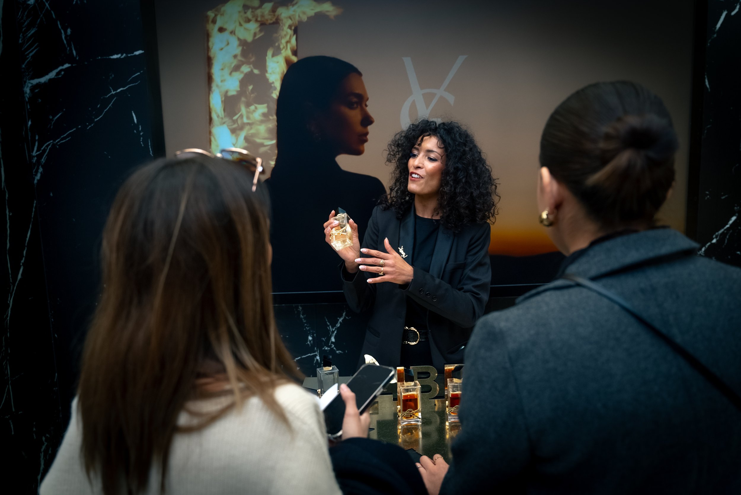 Femme expliquant un parfum à un groupe lors d'une présentation, avec affichage de produits de parfum sur la table.