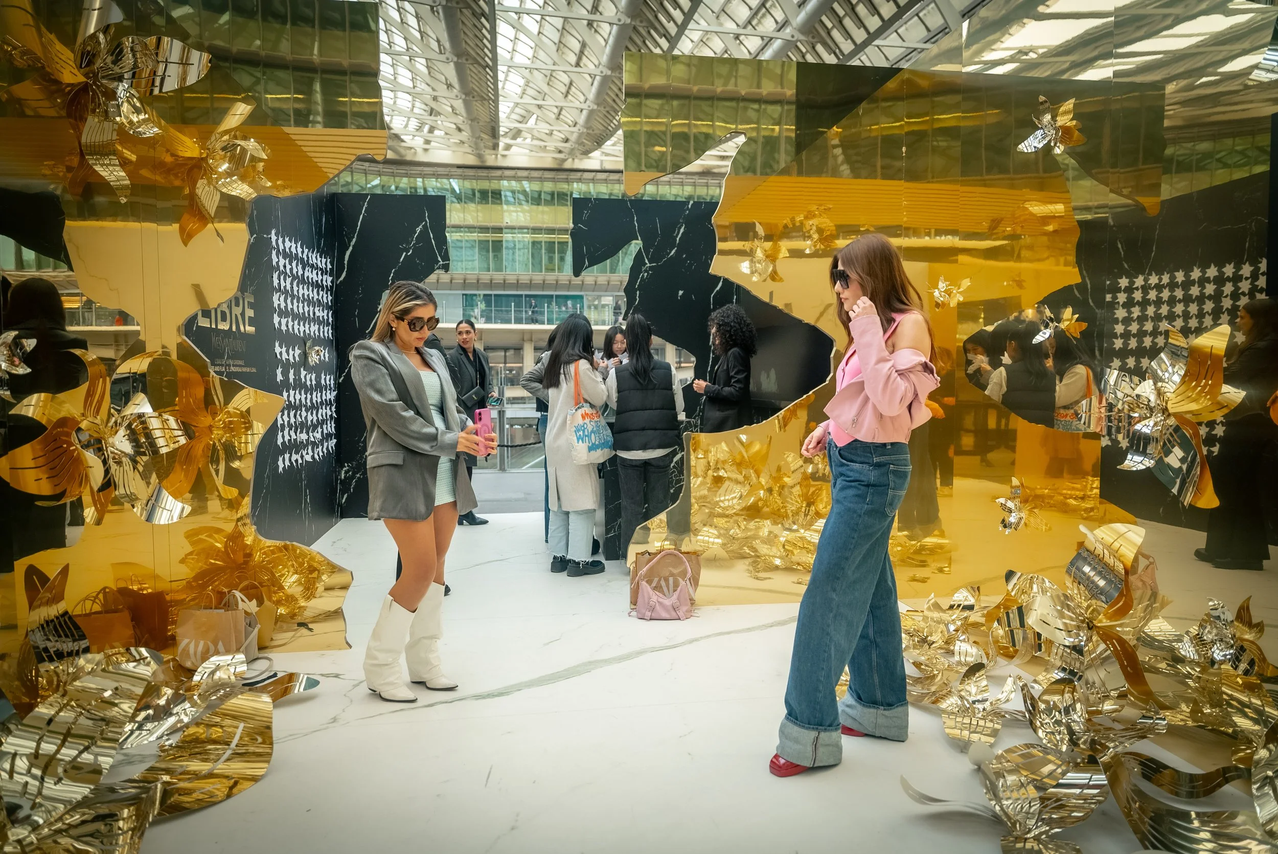 Groupe de personnes dans une installation artistique avec des murs en miroir doré et noir, décorations de papillons en métal doré.