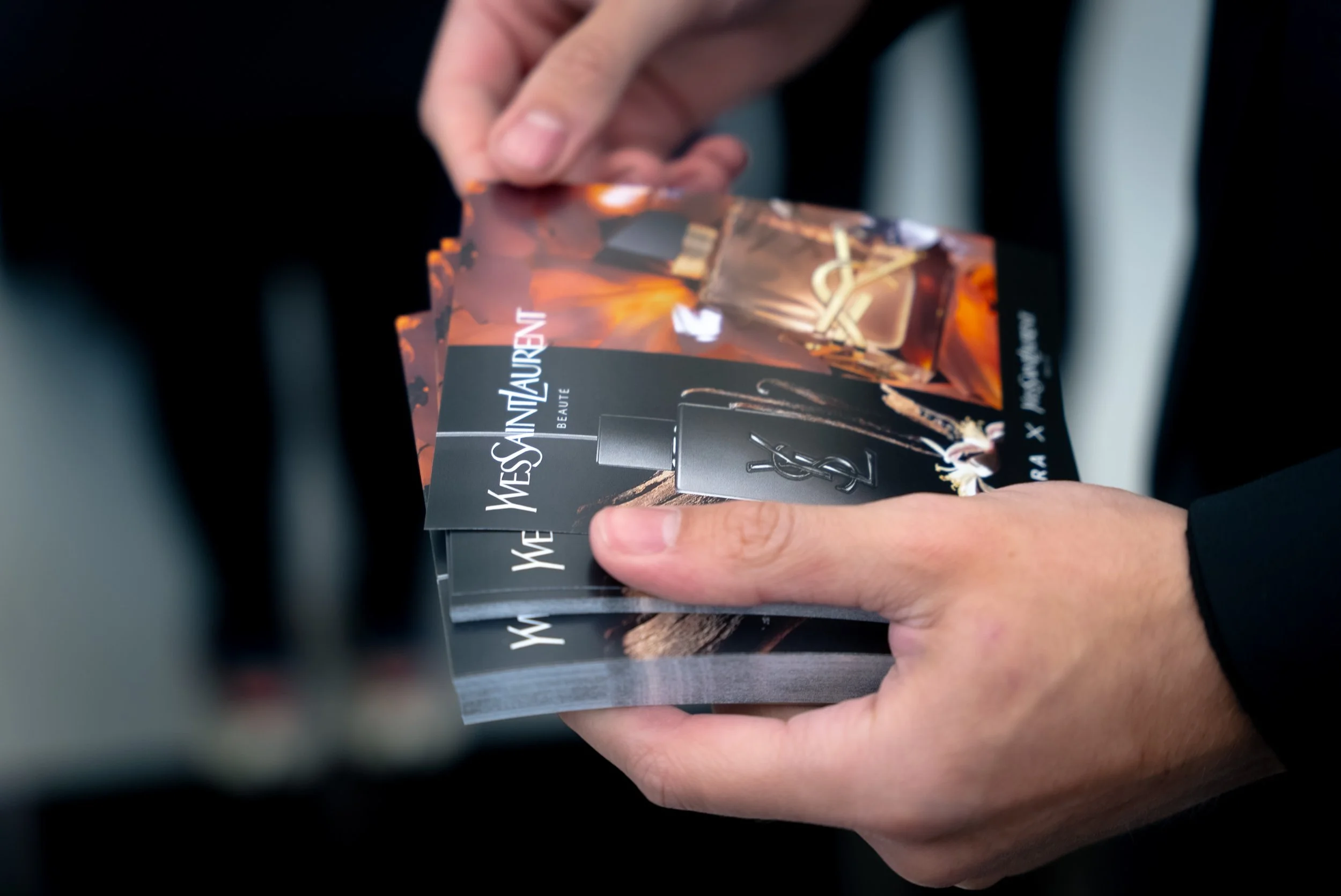 Une personne tenant une brochure promotionnelle pour Yves Saint Laurent Beauté avec une image de parfum