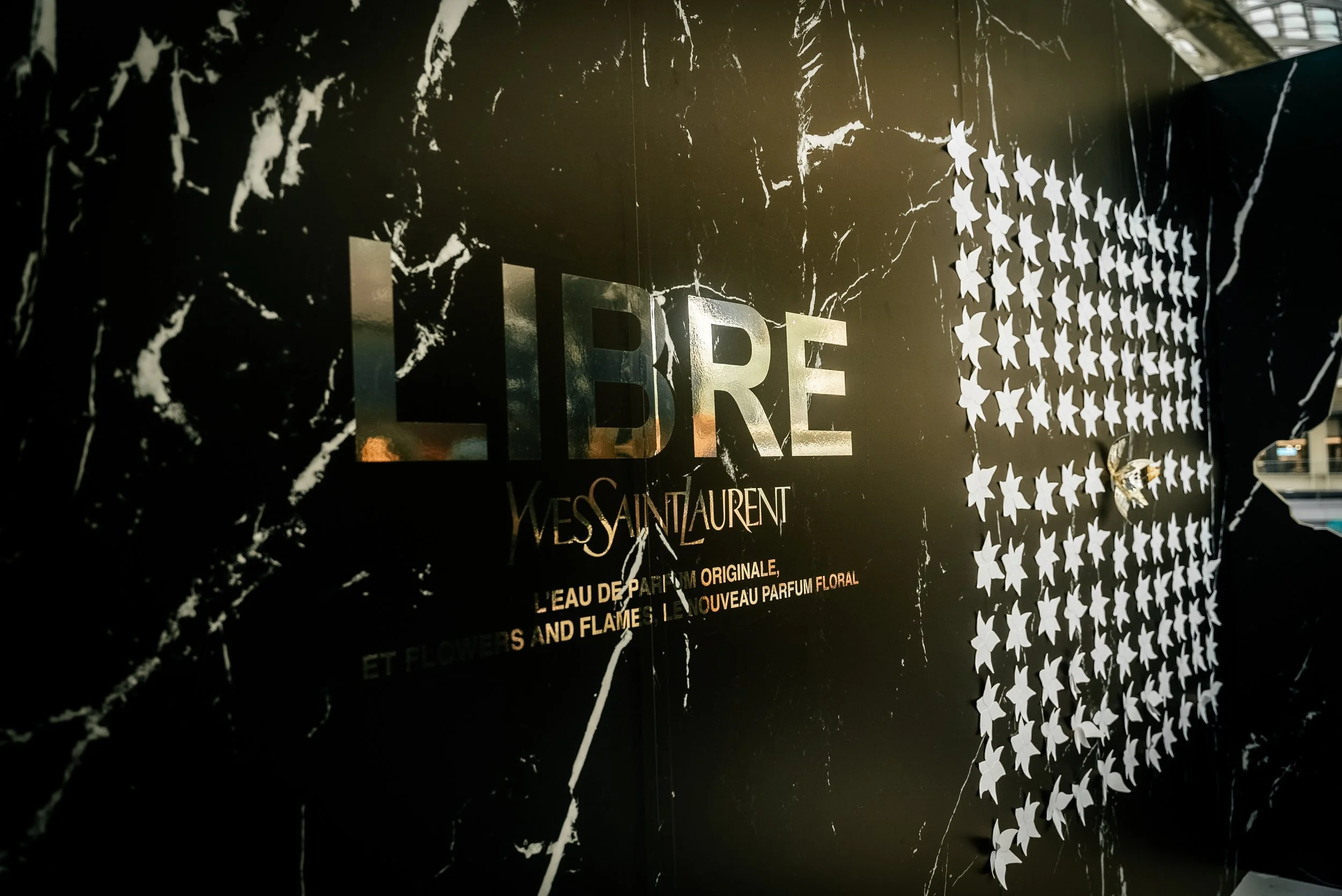 Affiche publicitaire pour le parfum Libre de Yves Saint Laurent, noire avec des étoiles blanches et du texte en lettres dorées.