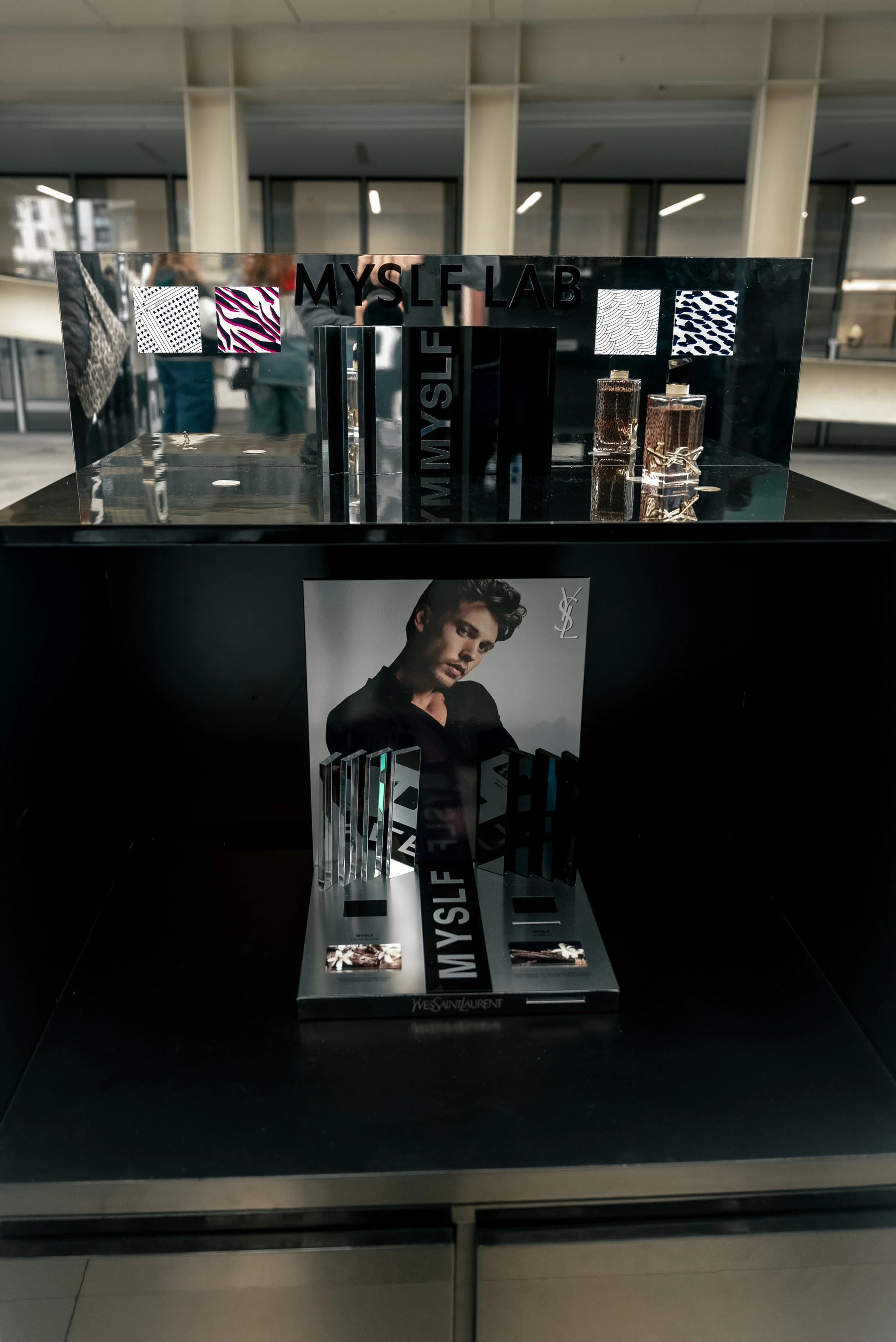 Publicité pour Yves Saint Laurent, présentant un modèle masculin et des flacons de parfum, avec des éléments de design en noir, blanc, et violet, et le texte 'MYSLF'.