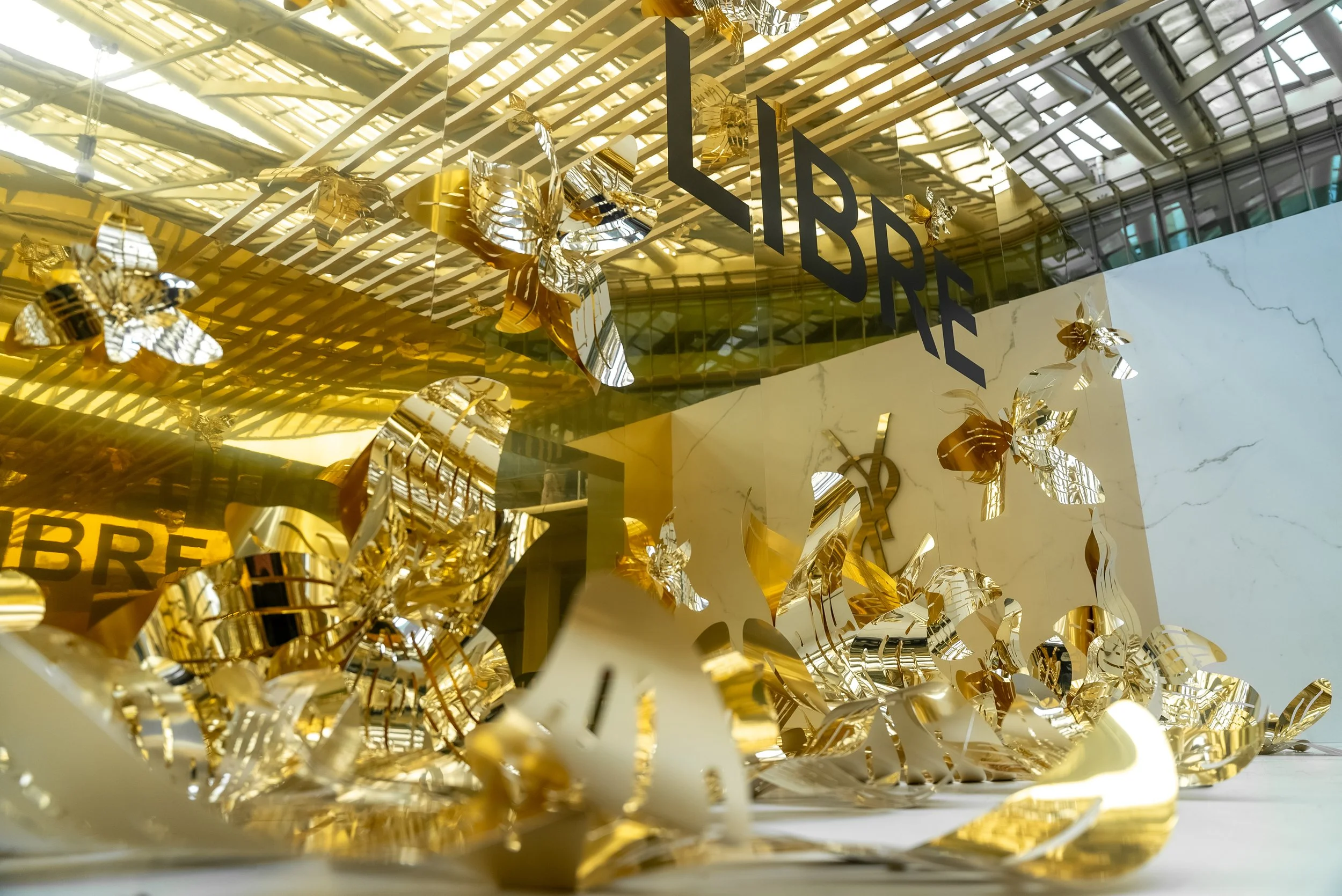 Vitrine d'une librairie avec décorations de papillons et fleurs en métal doré, reflet sur la façade en verre, inscription 'LIBRE' visible.