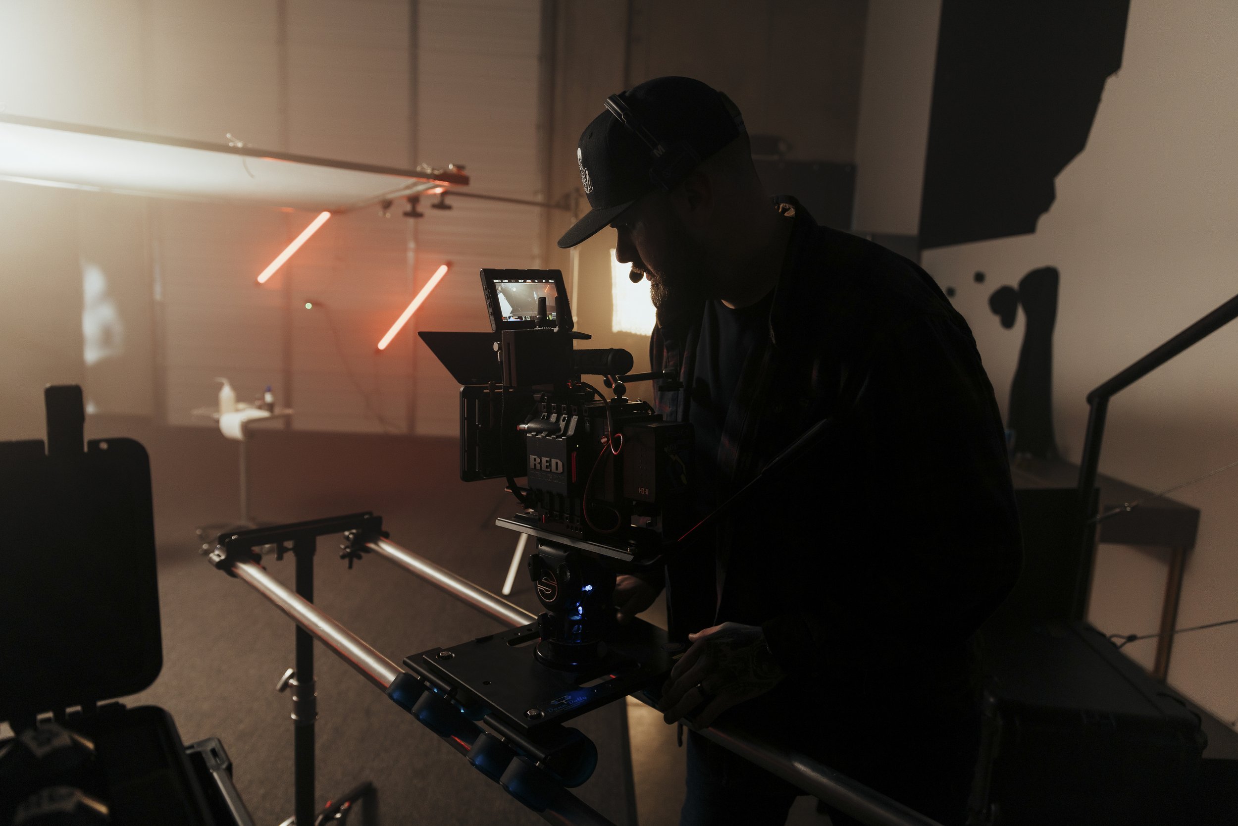 Silhouette of a person operating a camera on a filming set, with a dark background and neon lights.