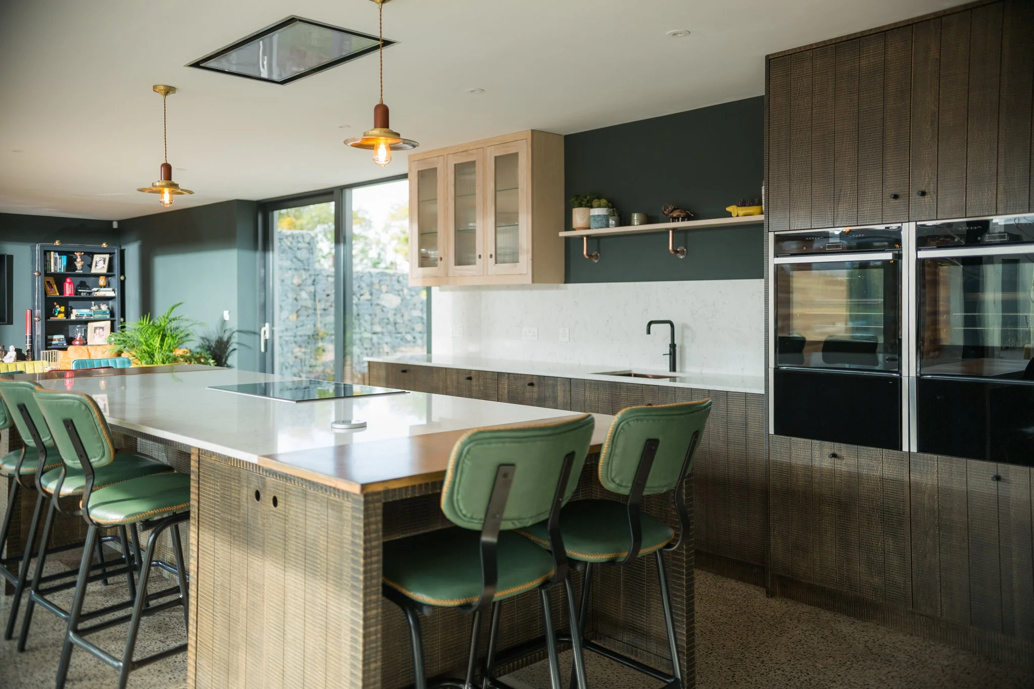 Contemporary completed kitchen with large island, green seating and dark bespoke cabinetry by Darren Morgan Design.