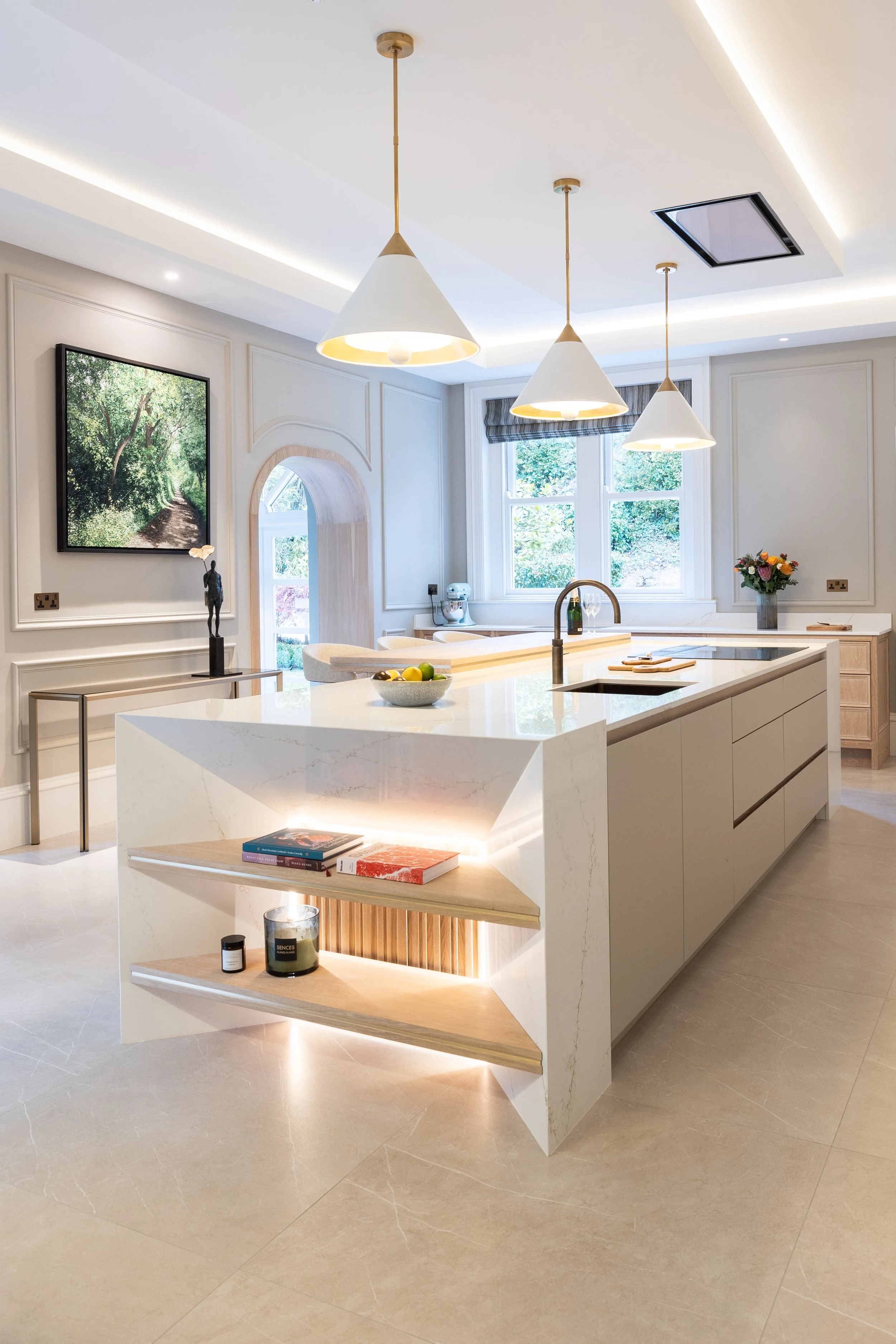 Bright contemporary kitchen with white island, integrated display shelving and pendant lights.