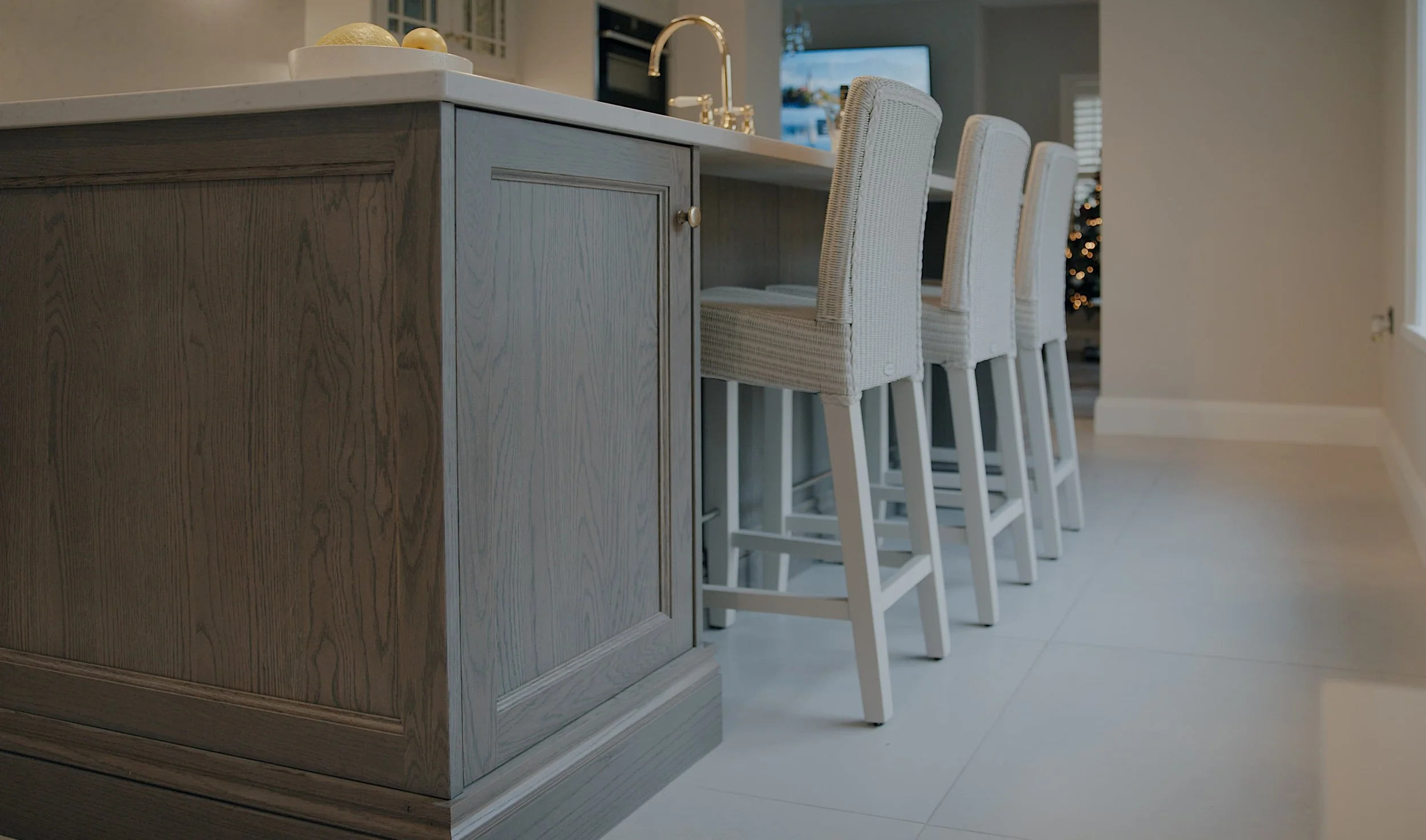 A low-down view of a bespoke kitchen island with three chairs tucked underneath, cabinets are grey wood with a white stone work surface - create from CGI properties and 3D animation