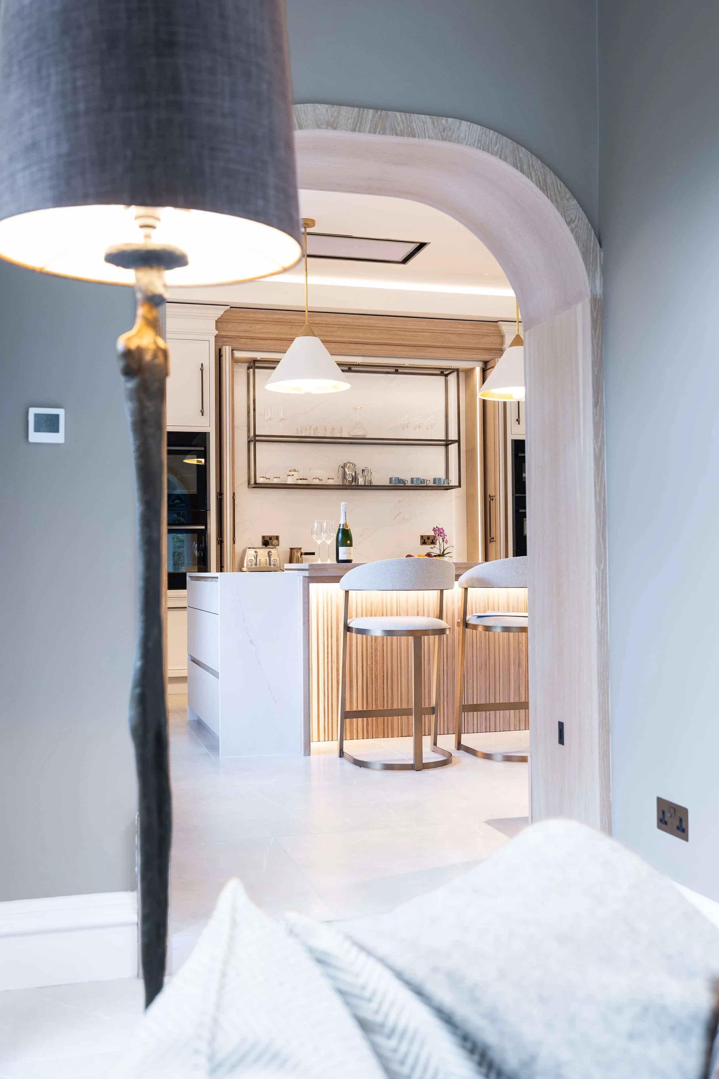 View through an arched opening into a completed luxury kitchen with island seating.