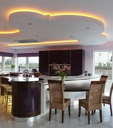 Curved kitchen island and dining area with layered ceiling lighting.
