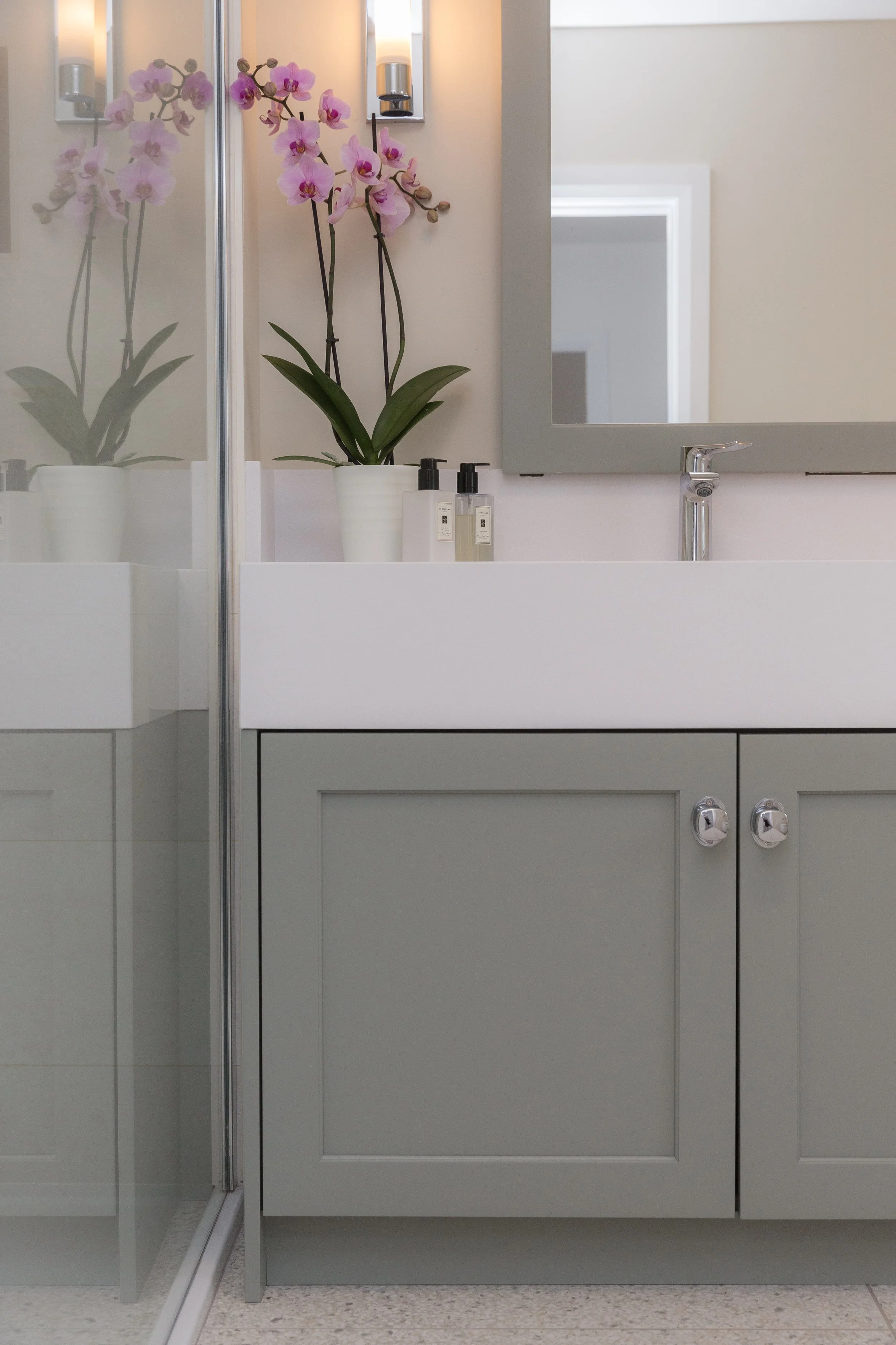 a low-down view of a greige bathroom cabinet with a white sink and hand soaps and a mirror above the sink