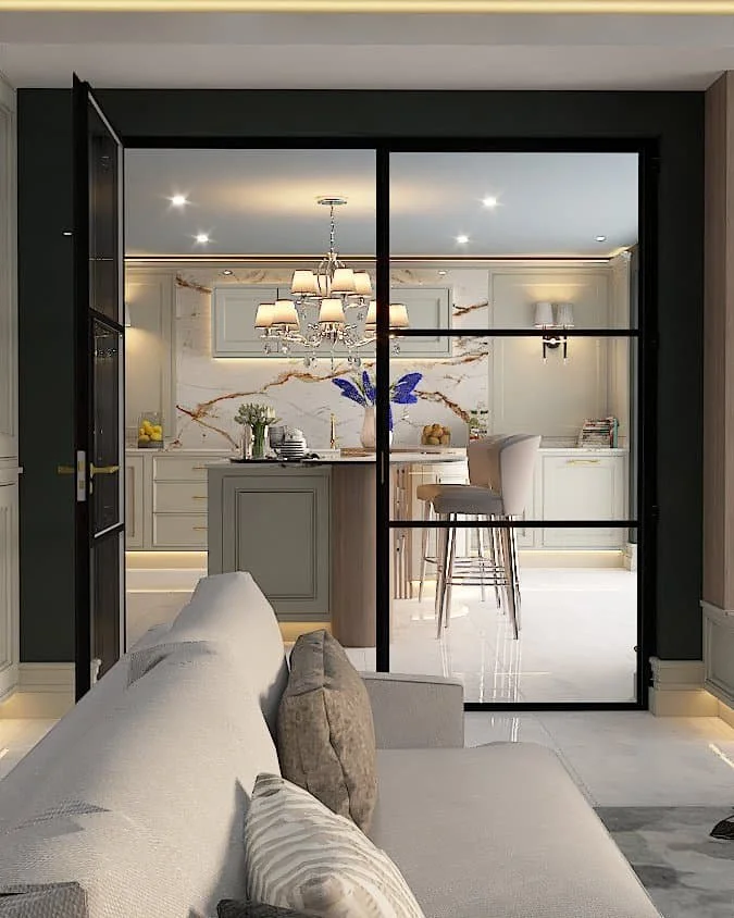 Looking through a living room with a cream sofa, through glass panel doors to a luxury white kitchen with a kitchen island a tall chairs - Darren Morgan Kitchens