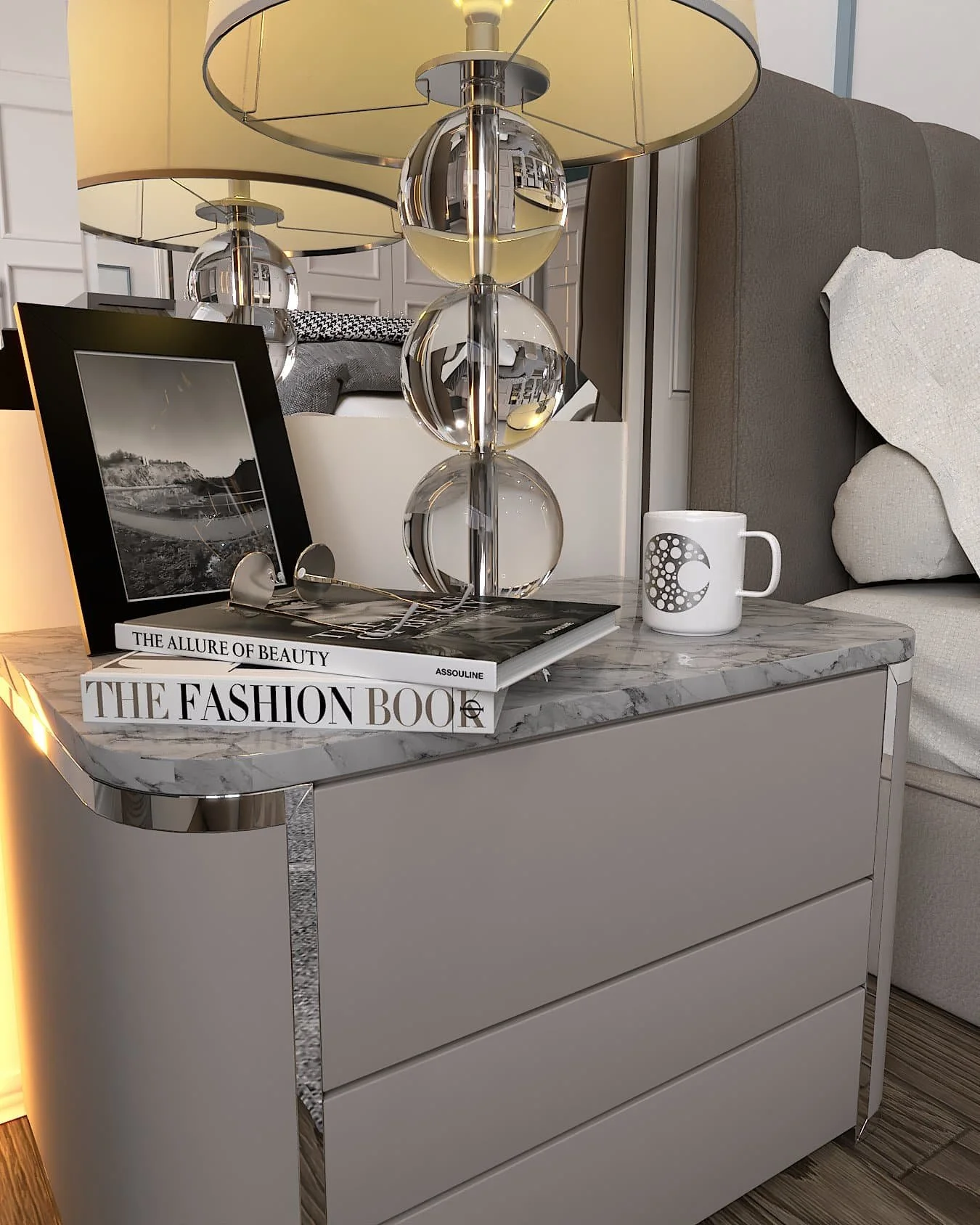 A grey, curved bedside table with chrome finishes and a grey marble surface. Two books, a black photoframe, a white mug and a glass lamp are on the table