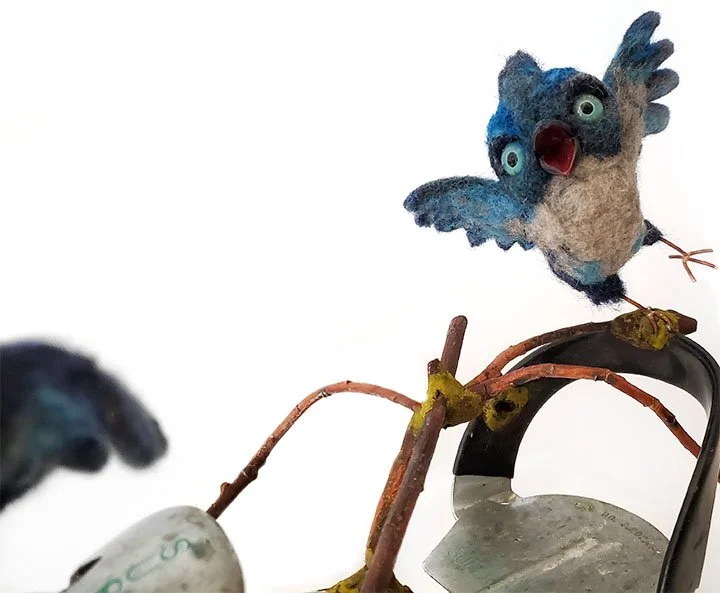 detail of two needlefelted baby blue steller's jays perched on a vintage metal roller skate with branches