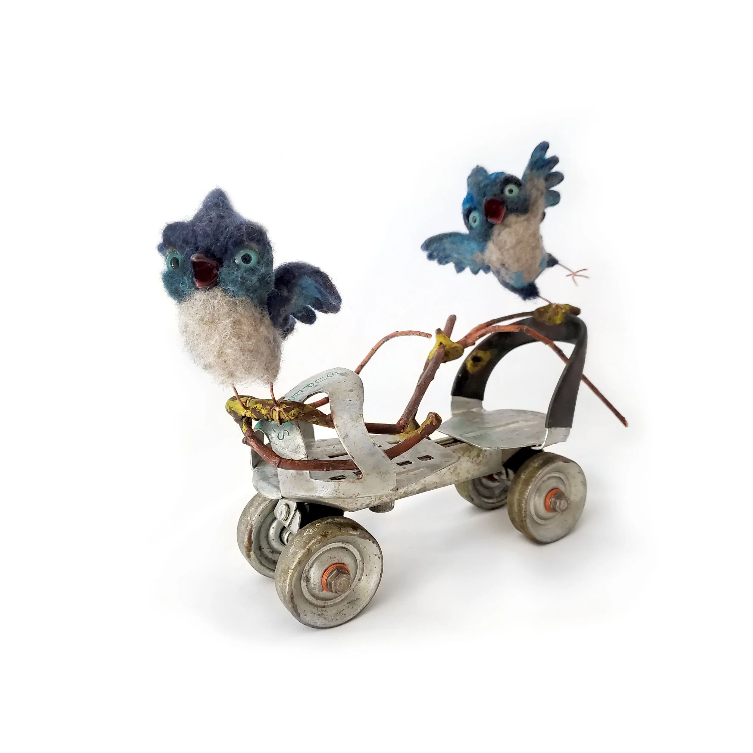 mixed media sculpture of two baby steller's jays riding on a vintage metal roller skate