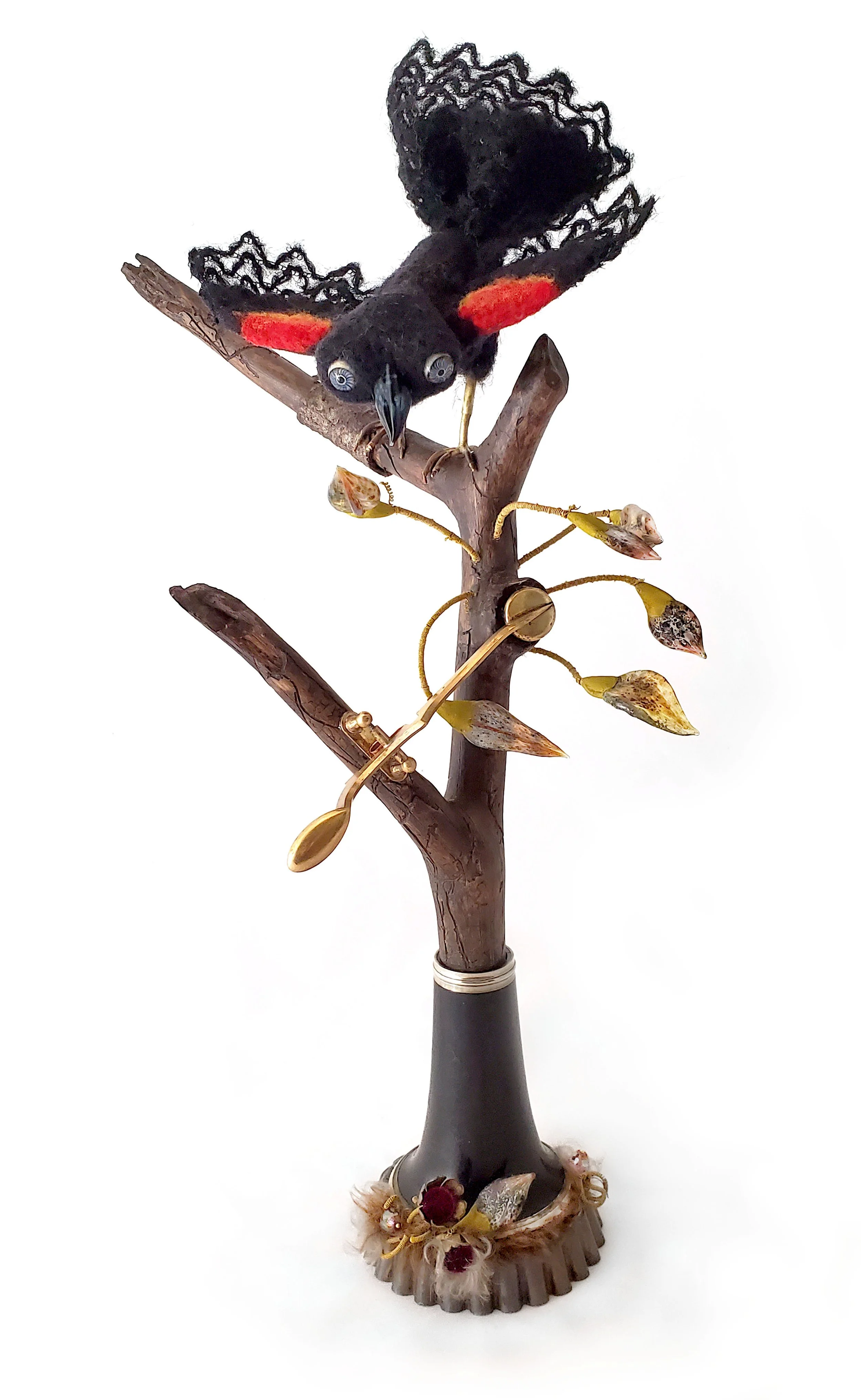 mixed media sculpture of redwinged blackbird on a tall branch with flamworked glass leaves, the branch is growing out of an antique clarinet bell, there is a saxophone key growing out of the branch