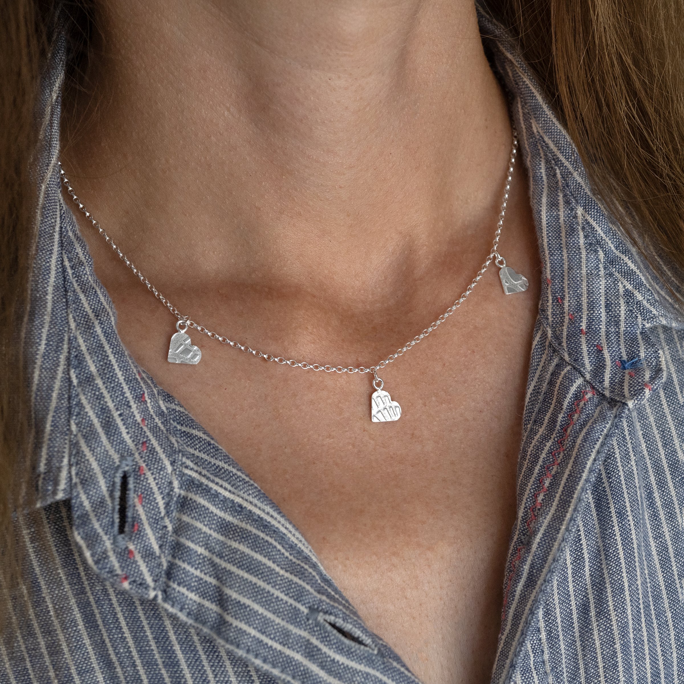 A side view of a person wearing a silver three heart textured necklace against a blue and white dress.
