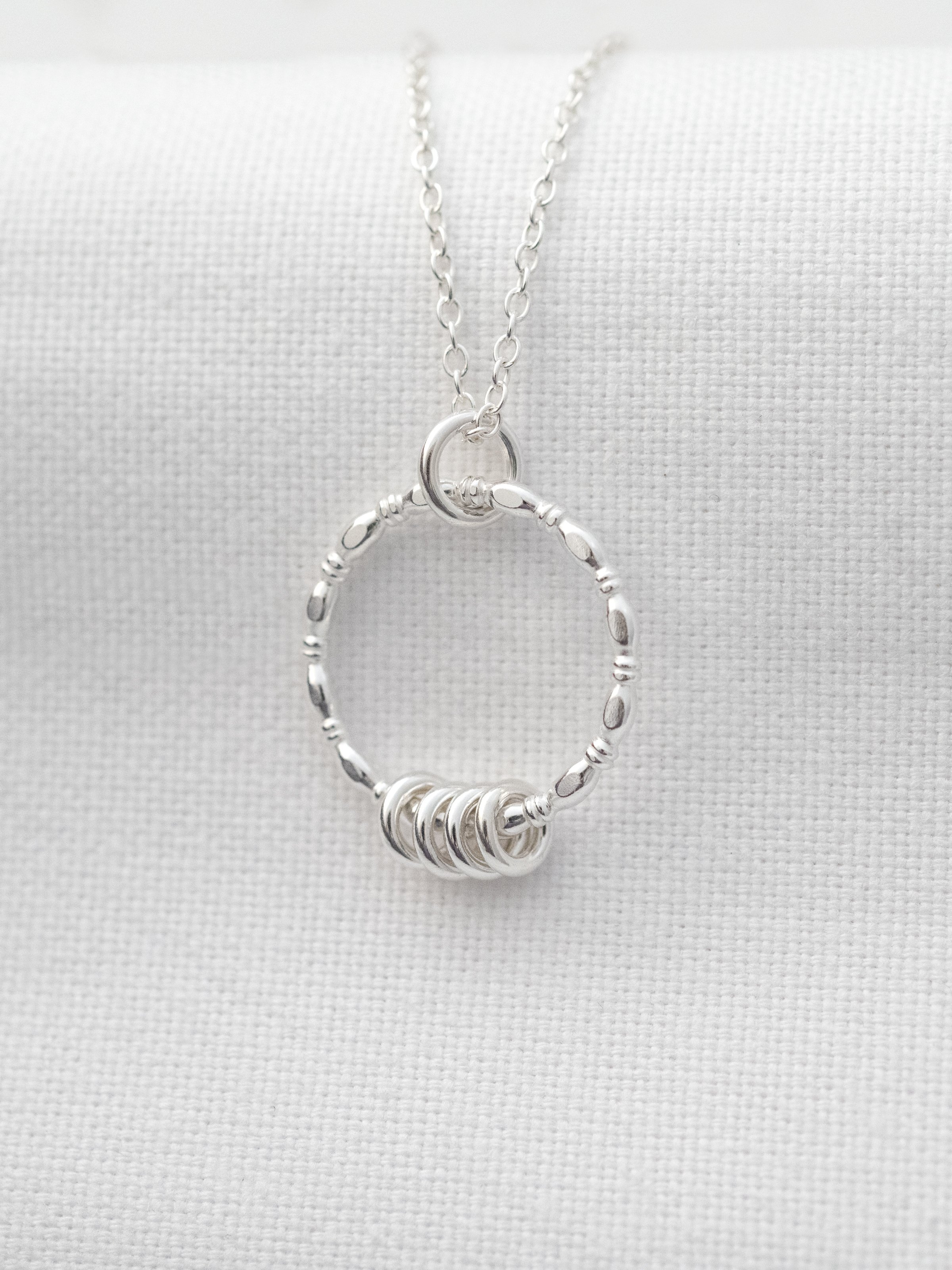 A Close up of a silver 40th birthday necklace displayed on white material.