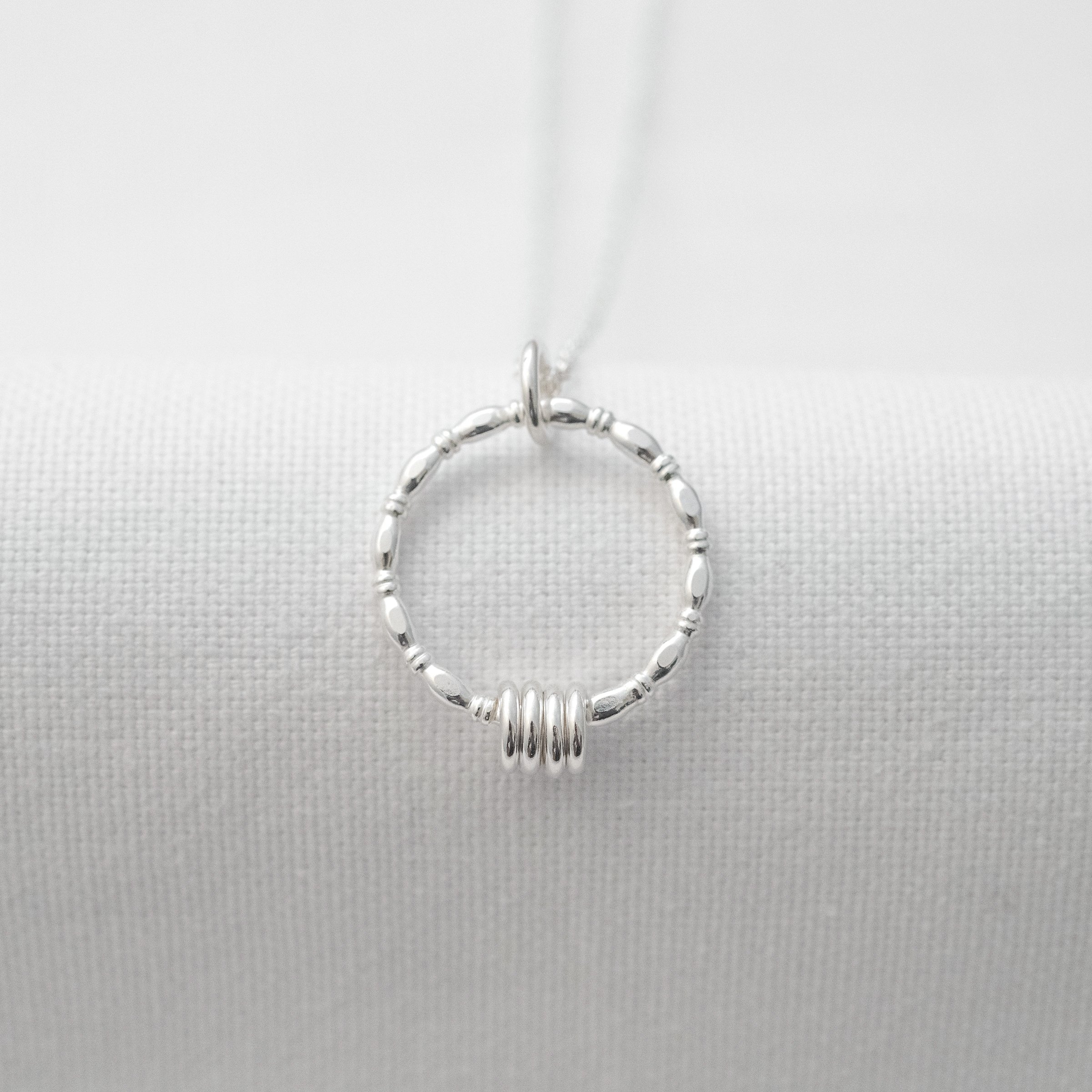 A front view of a sterling silver 4 ring birthday necklace displayed over white material.