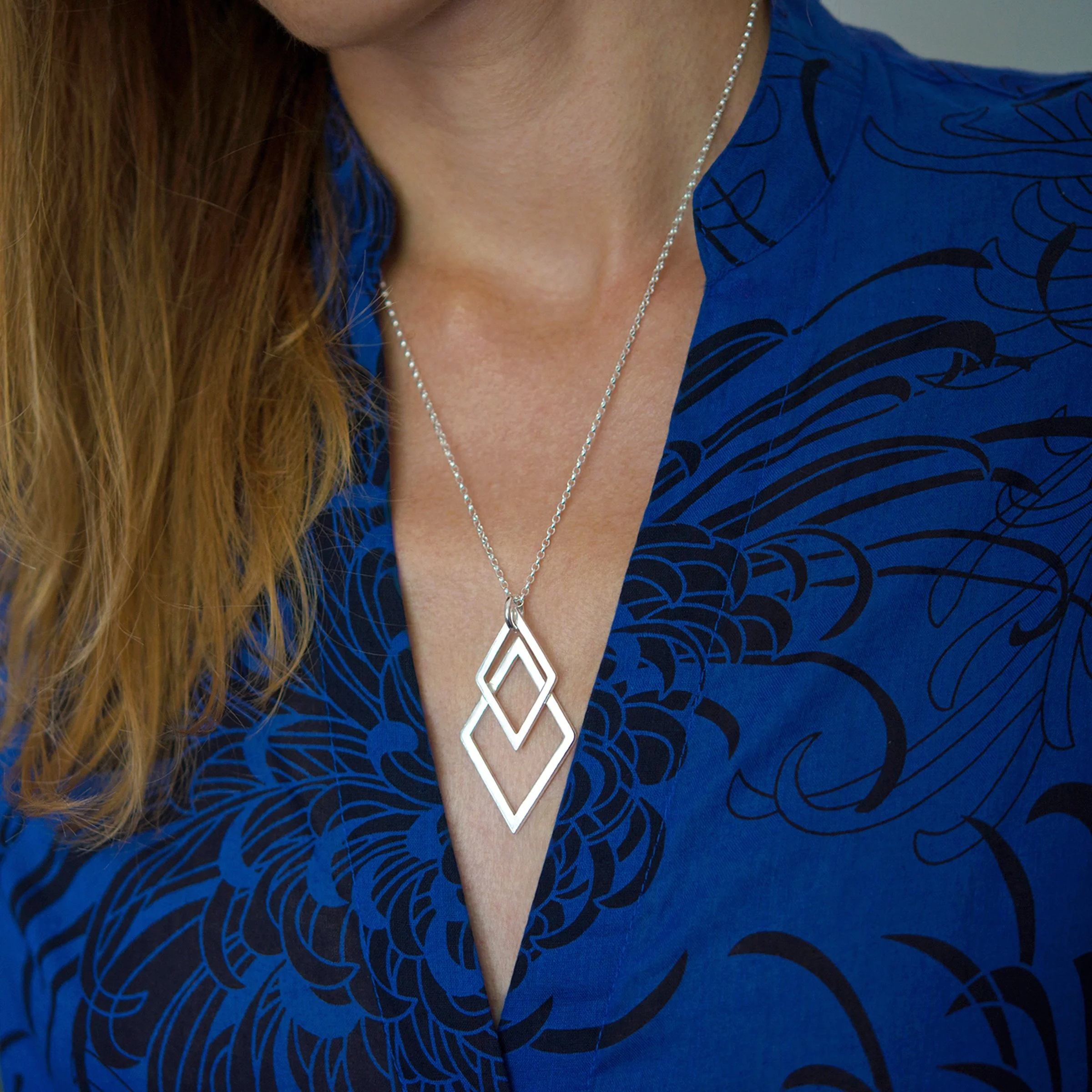 A person wearing a sterling silver unique geometric necklace against a blue dress.