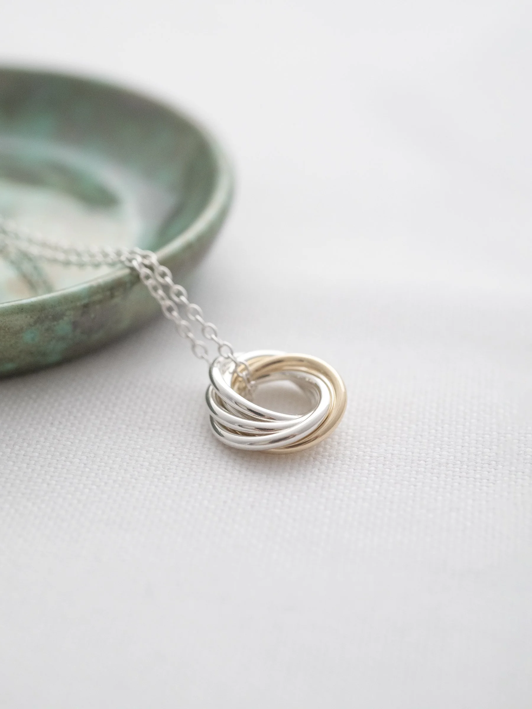 A side view of a 50th birthday necklace displayed on white material with a green jewellery dish in the background.