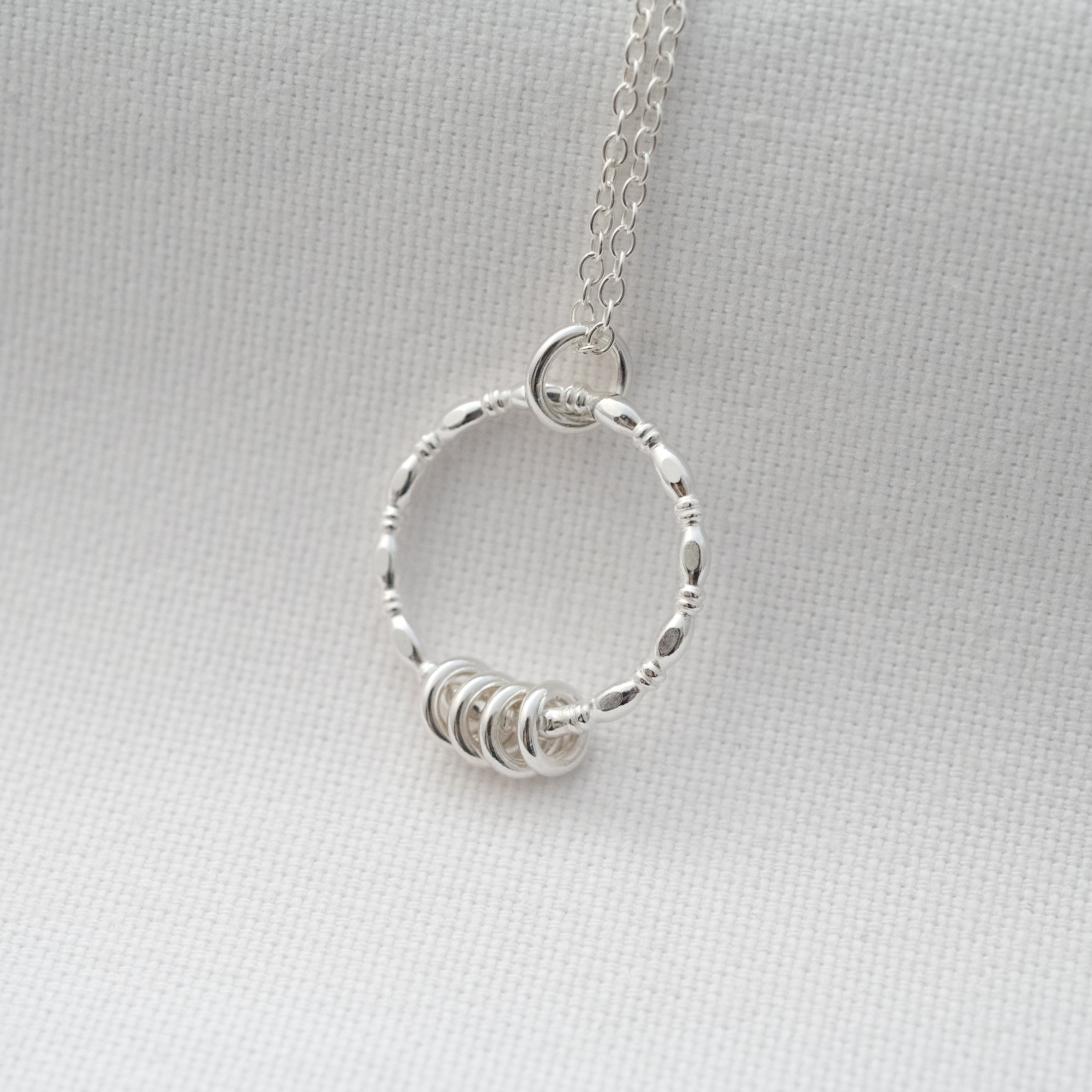 A side angle of a silver 4 ring necklace displayed over white material.