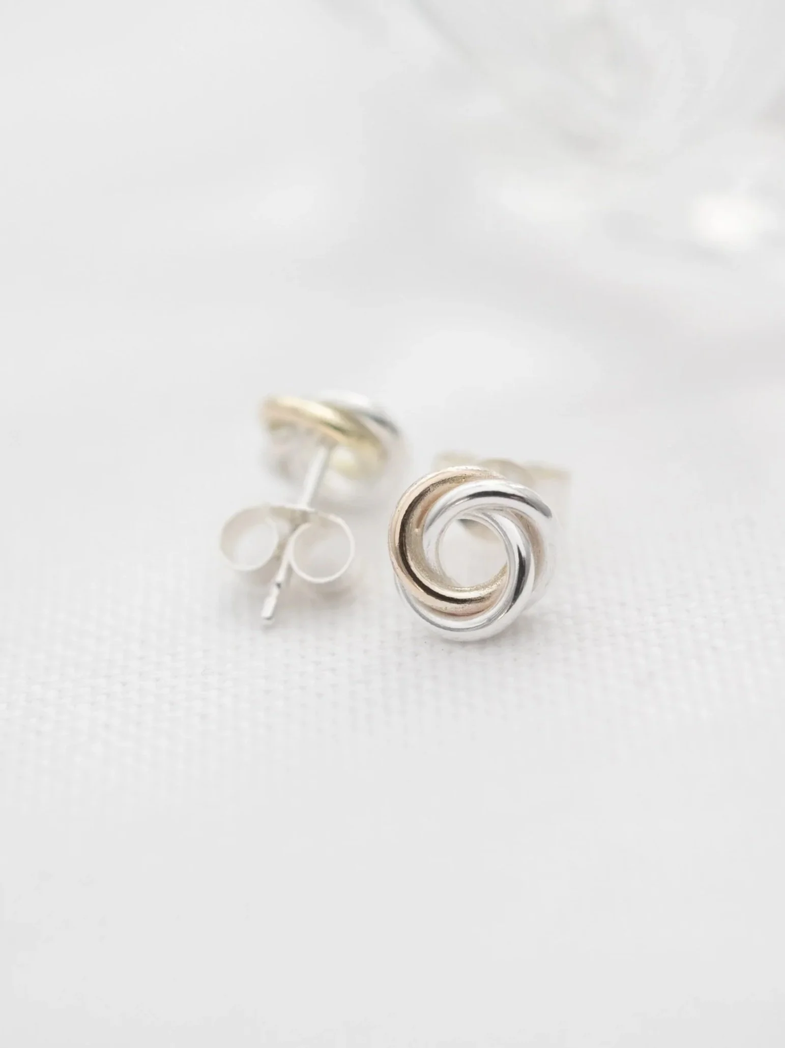 A front and back view of gold and silver interlinked stud earrings displayed on white material.