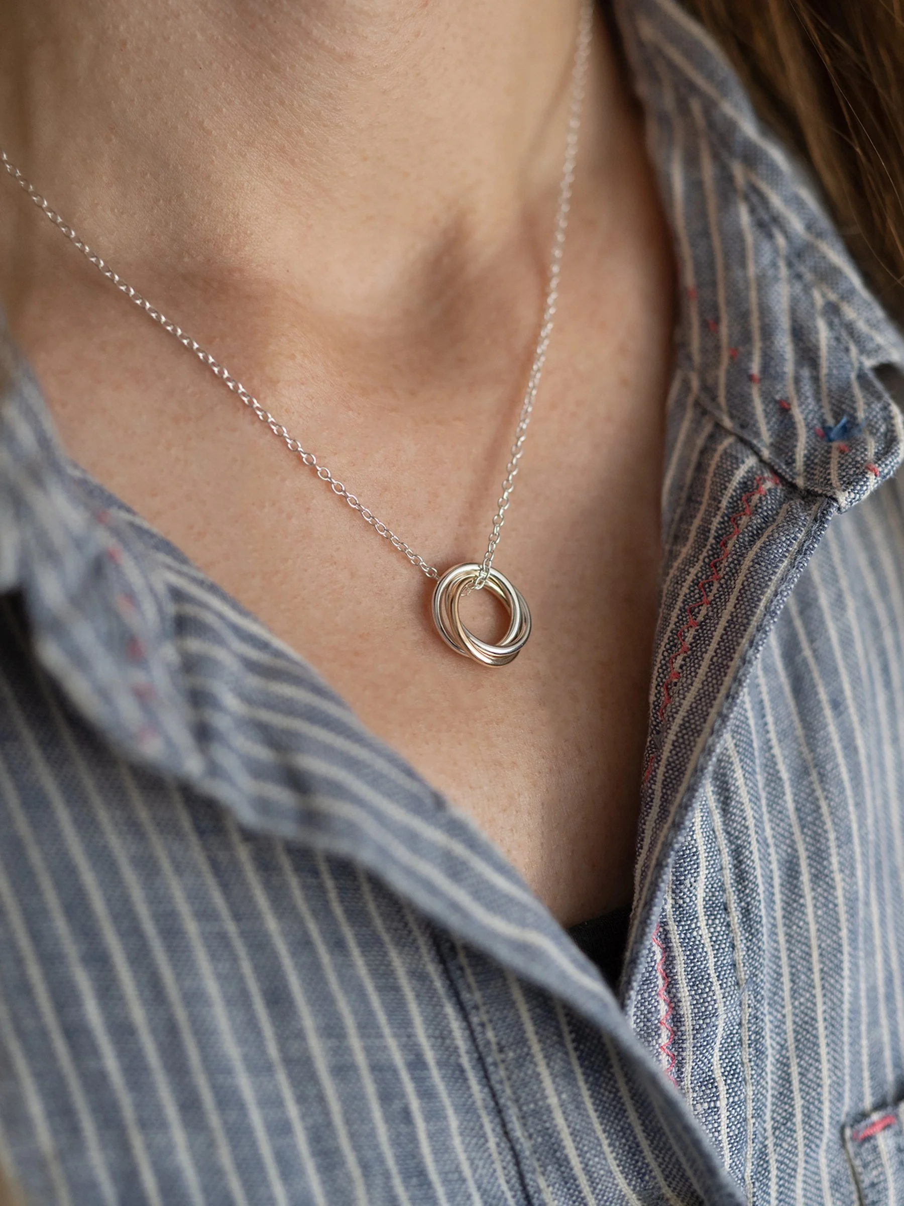 A side view of a person wearing a 30th gold and silver birthday necklace against a blue and white striped dress.