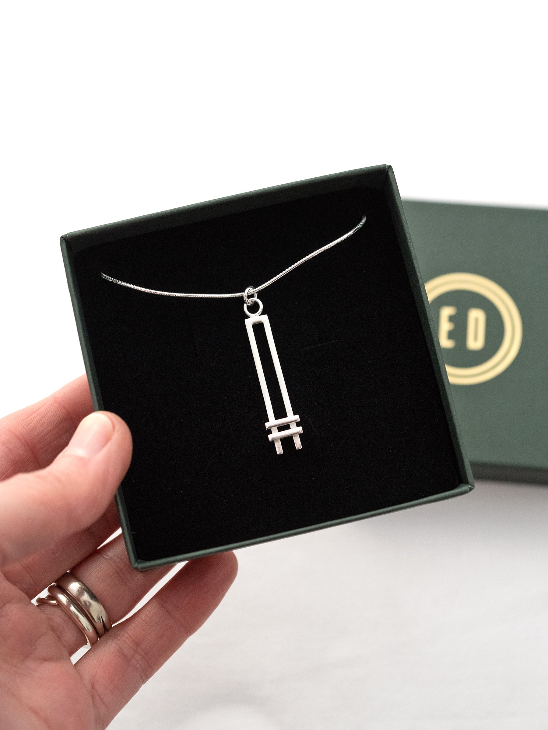A silver Art Deco style necklace displayed in a jewellery presentation box.