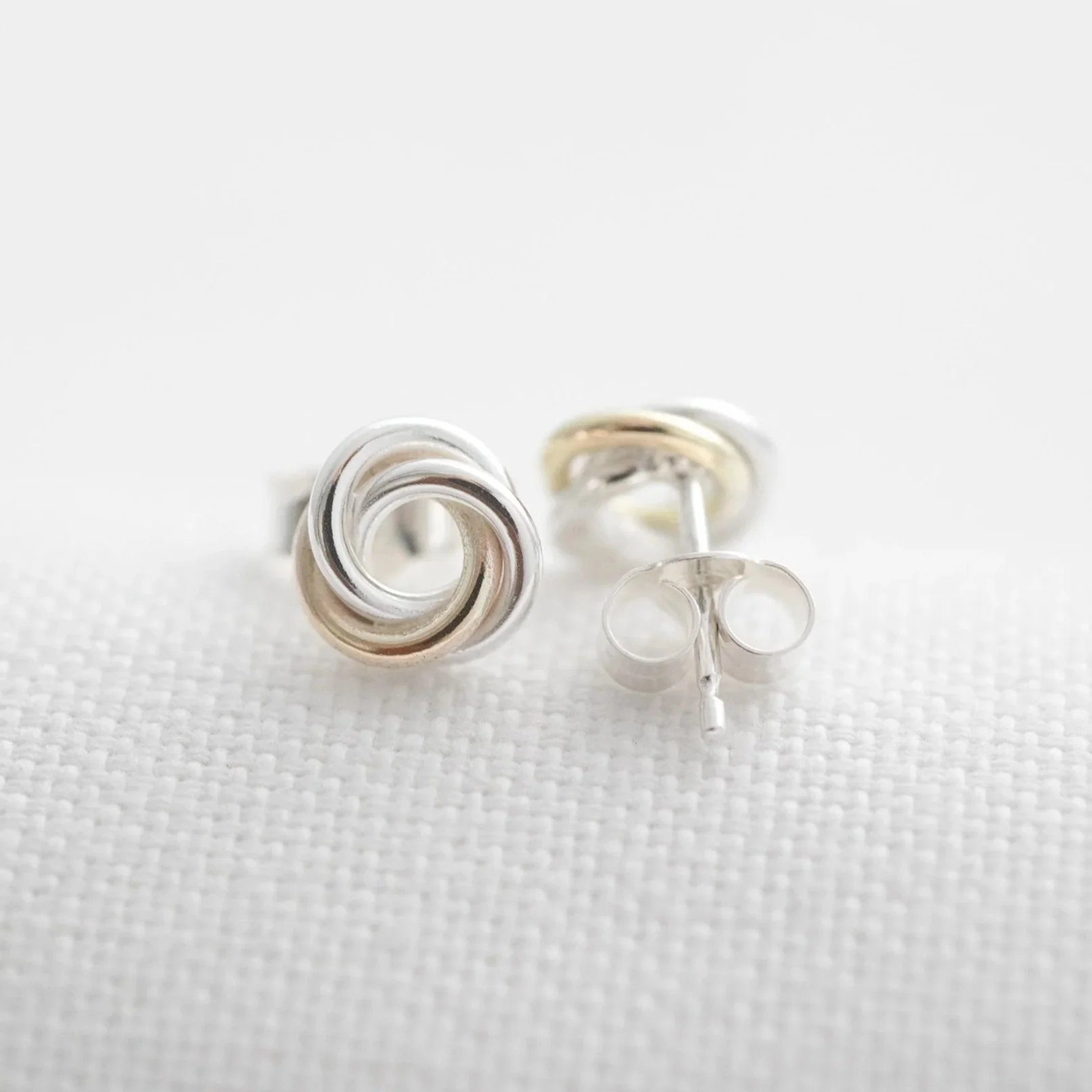 A pair of gold and silver Russian ring stud earrings displayed on white material.