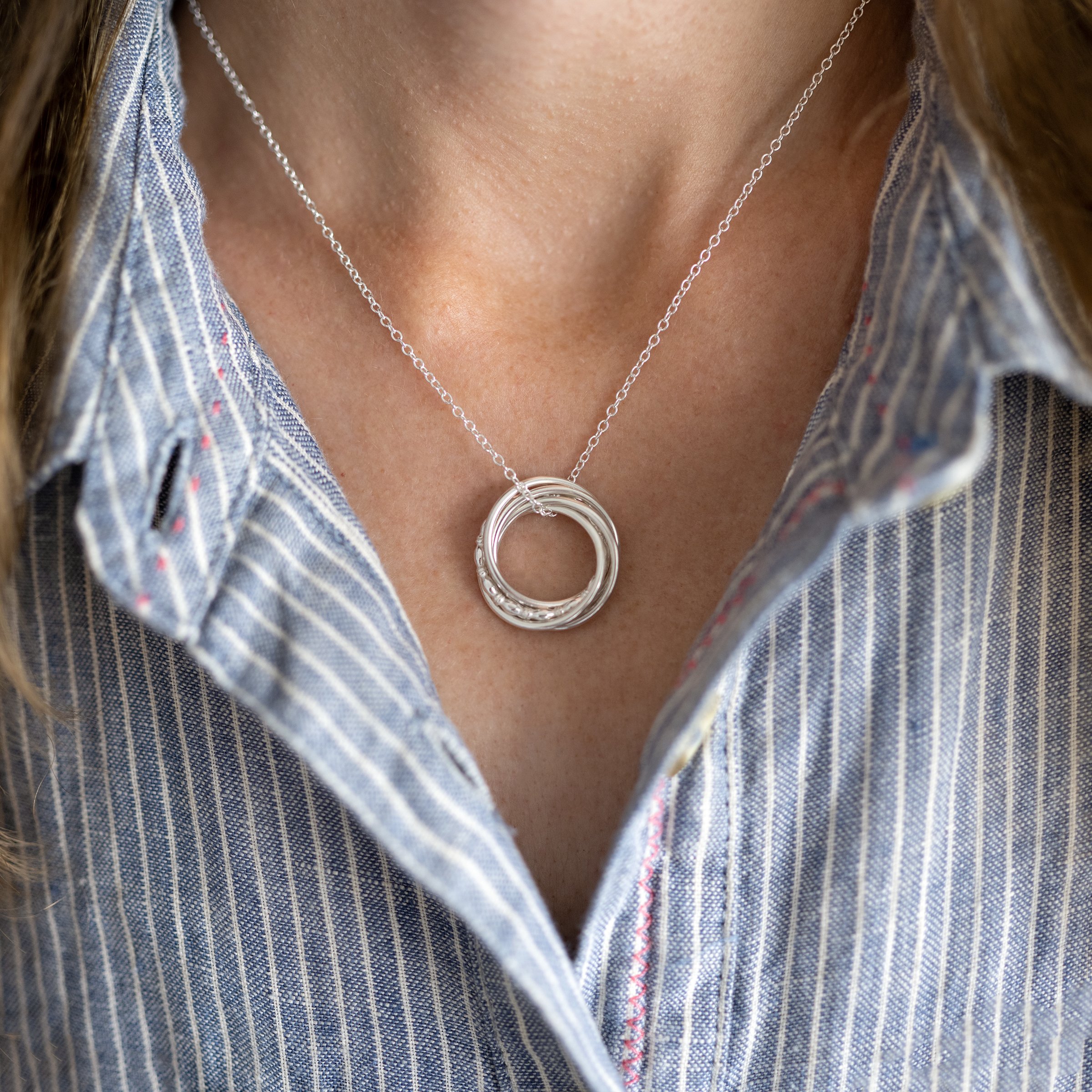 A person wearing a silver 50th birthday ring necklace against a blue and white dress.