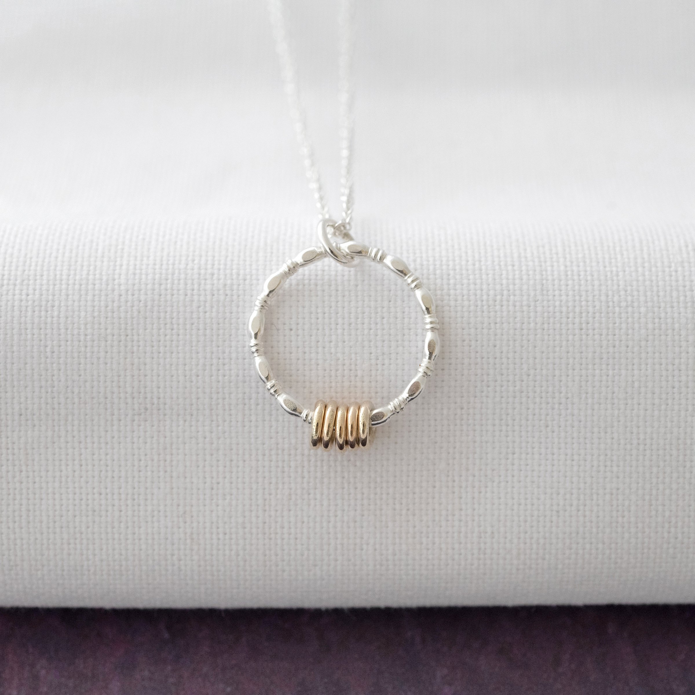 A five ring gold and silver necklace hanging over white material against a purple background.