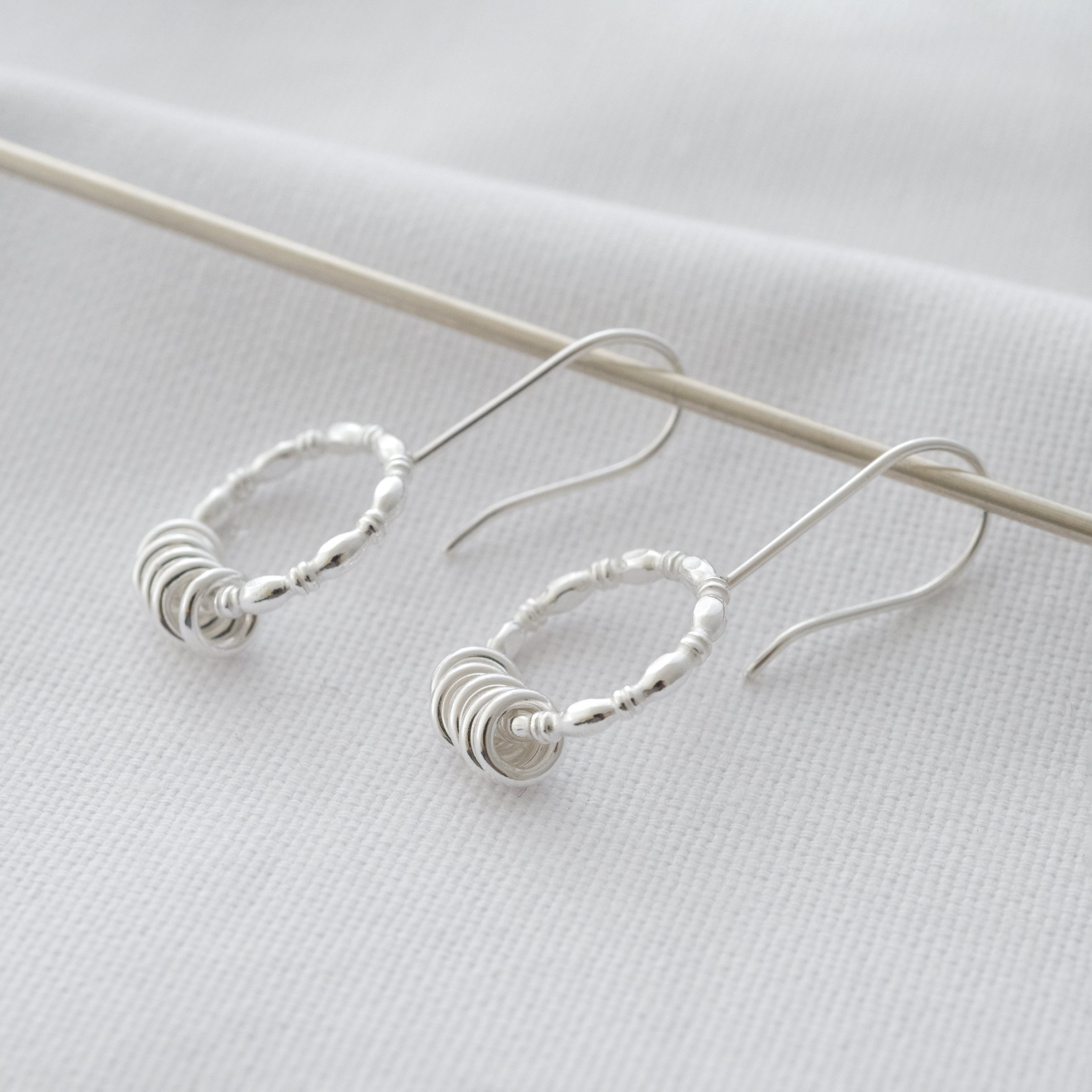 A side view of a pair of five ring earrings displayed over white material.
