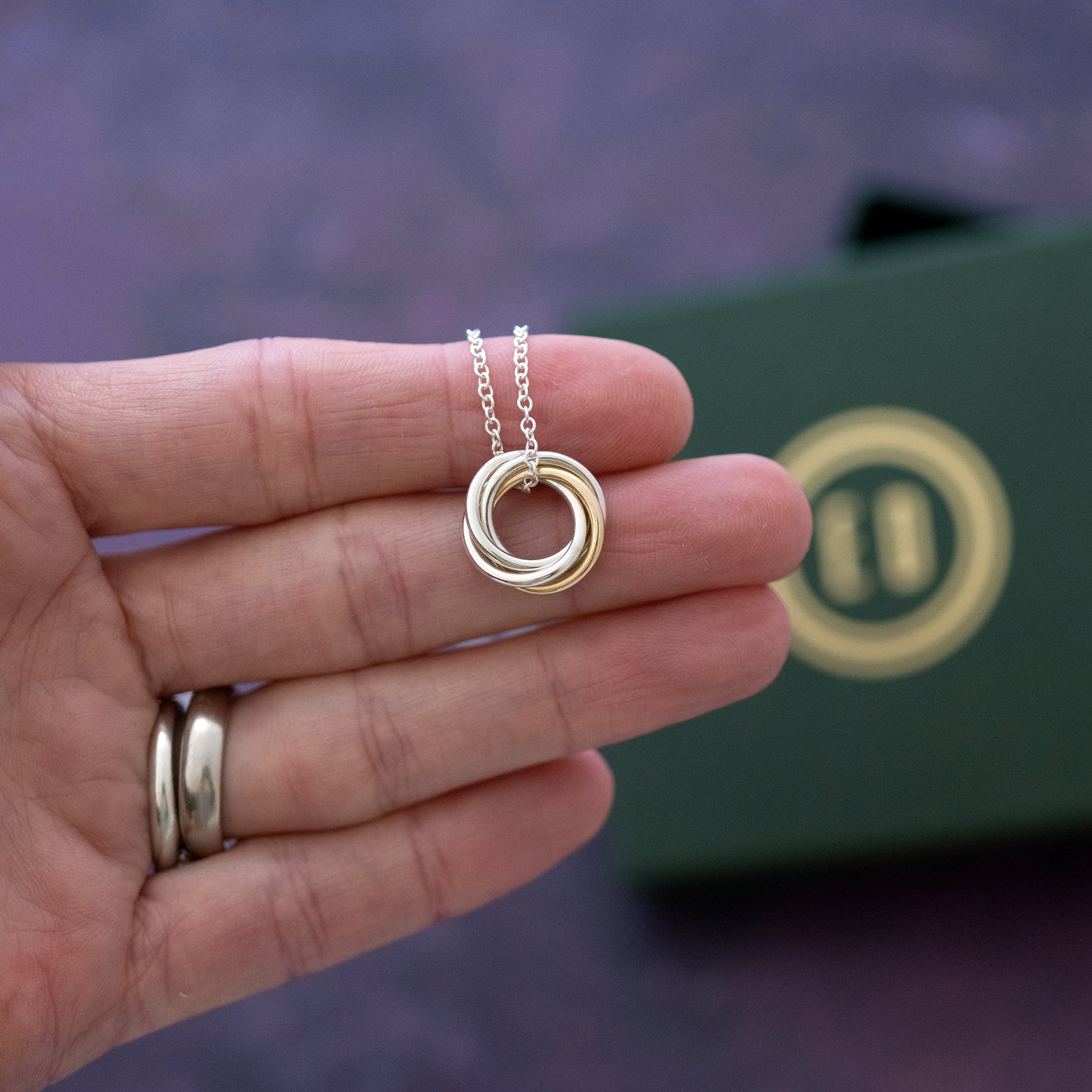 A gold and silver 40th birthday necklace displayed on a persons hand with the presentation box in the background.