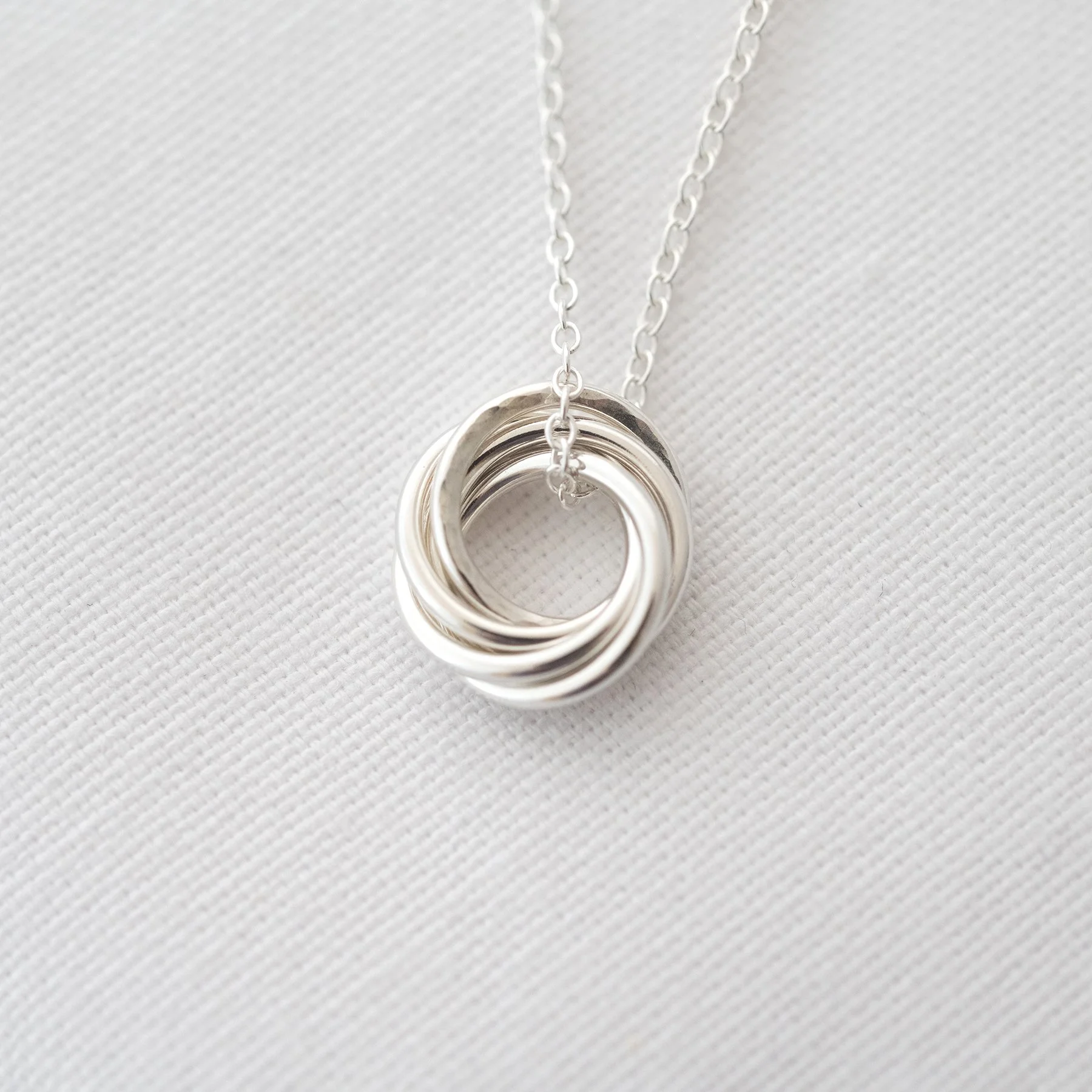 A close up of a 5 ring silver necklace displayed over white material.