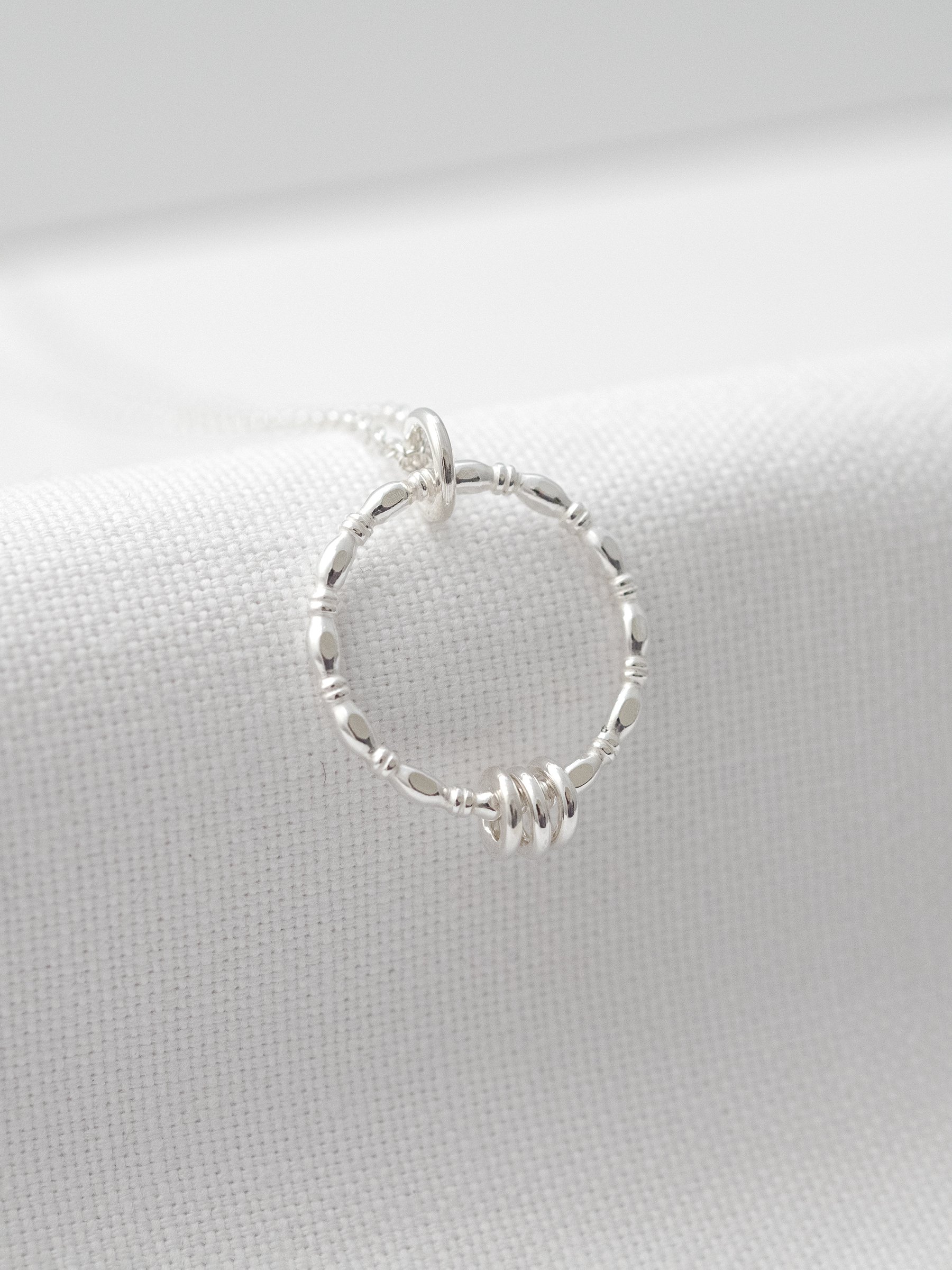 A close up of a sterling silver 30th birthday necklace hanging over white material.