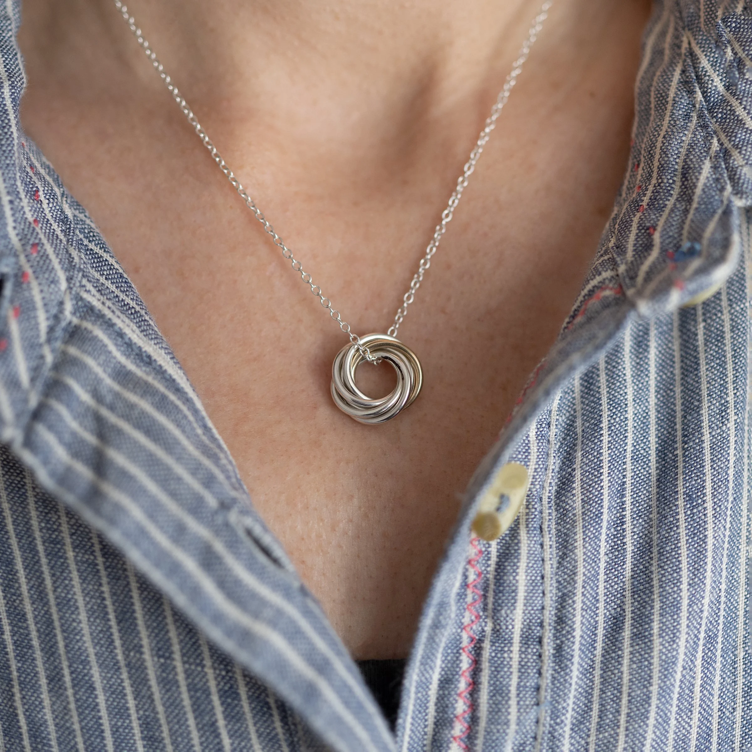 A close up of a person wearing a gold and silver 60th birthday necklace against a blue and white striped dress.