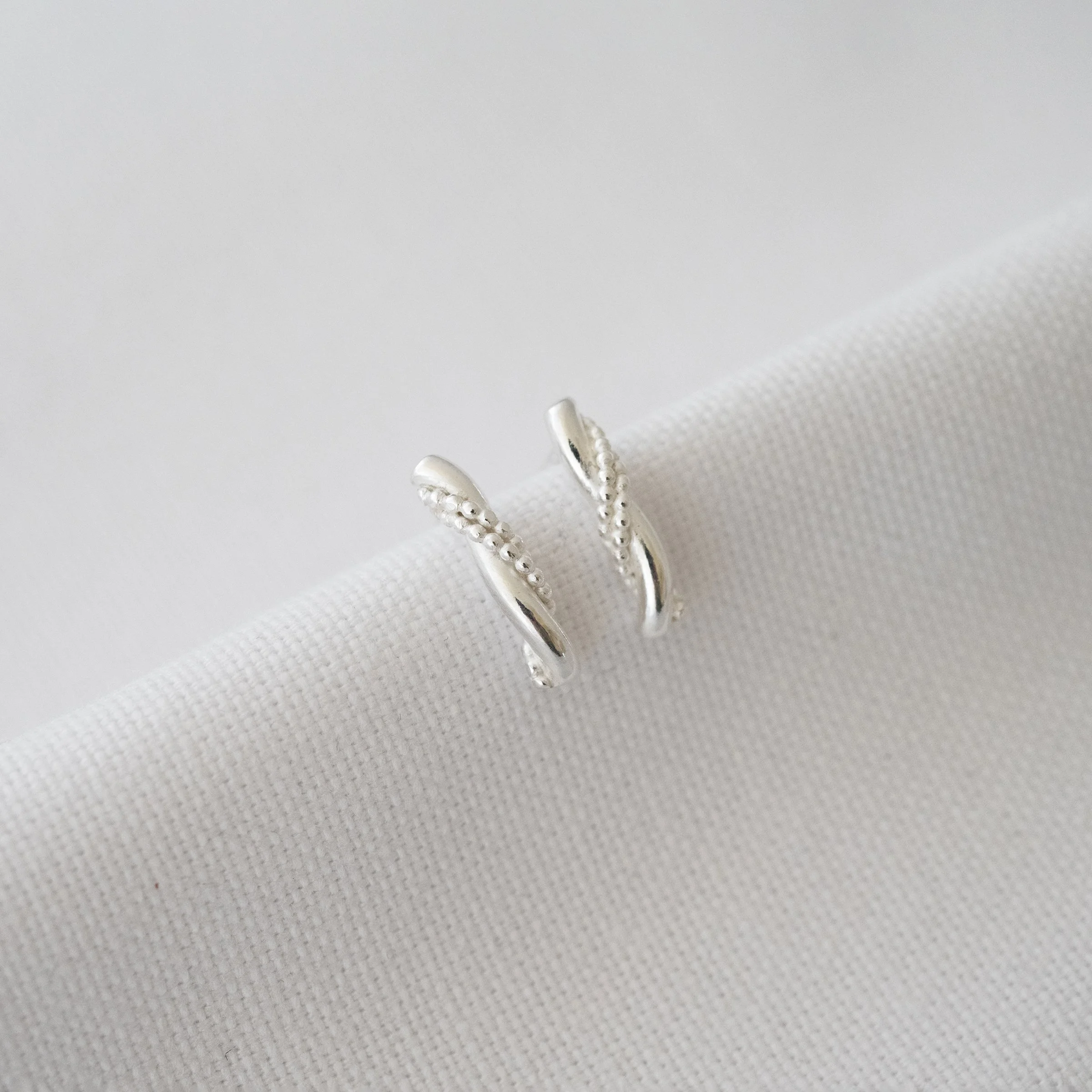 A pair of sterling silver short bar stud earrings displayed over white material.