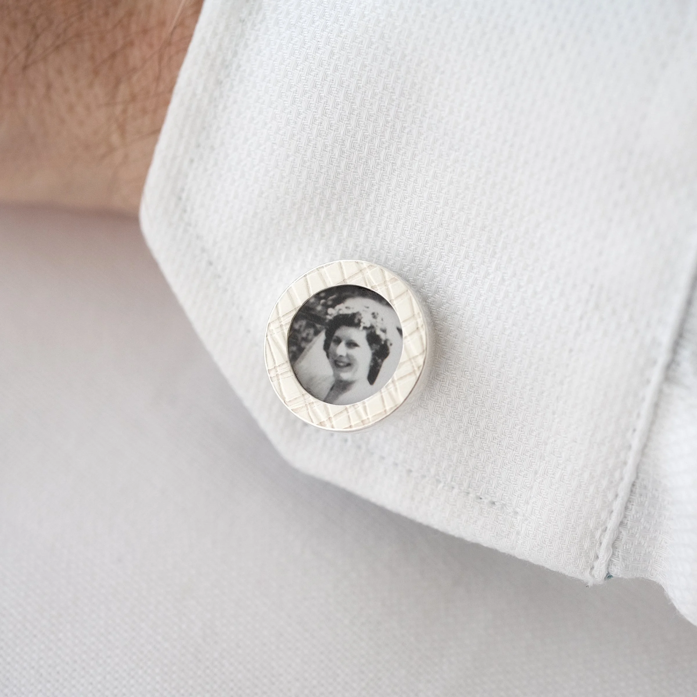 A silver photo cufflink positioned in a white shirt.