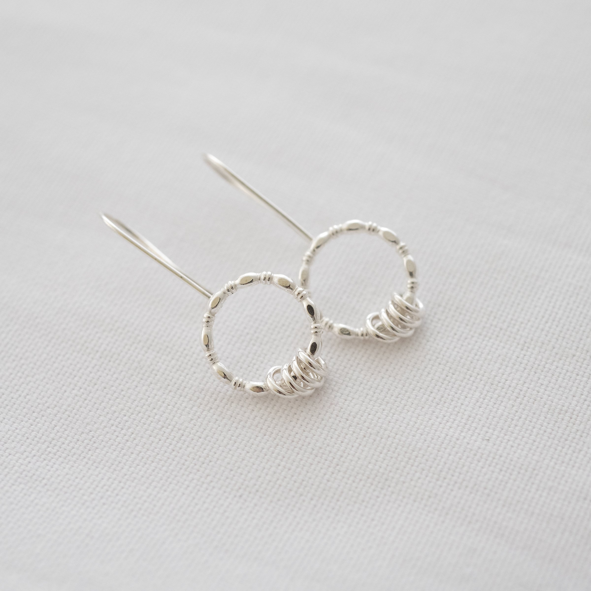 A pair of sterling silver circle earrings laid on their side on white material.