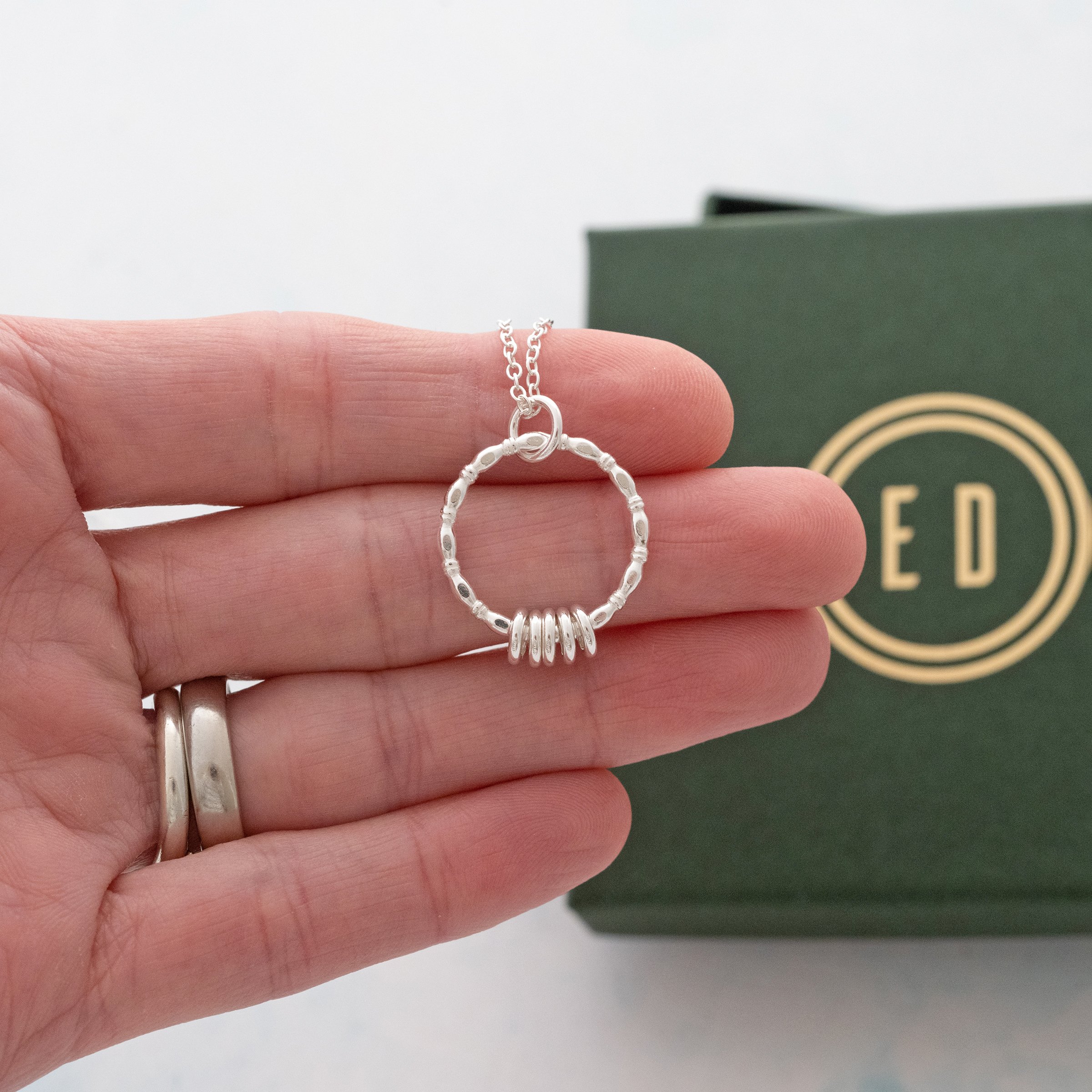 A silver 50th birthday necklace displayed on a persons hand with the presentation box in the background.